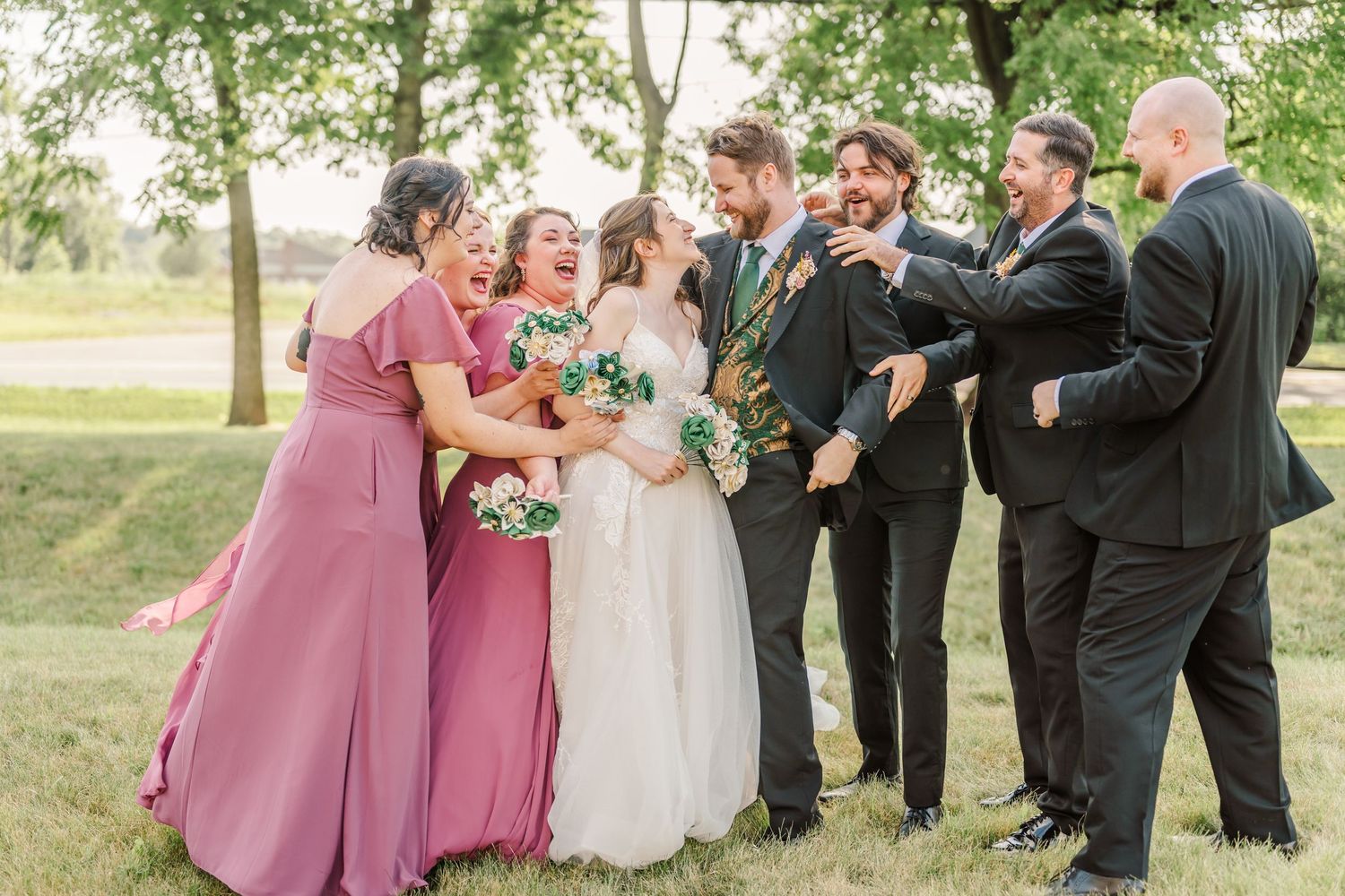 Wedding party posing outdoors with bridesmaids in dusty rose dresses and groomsmen in dark suits.