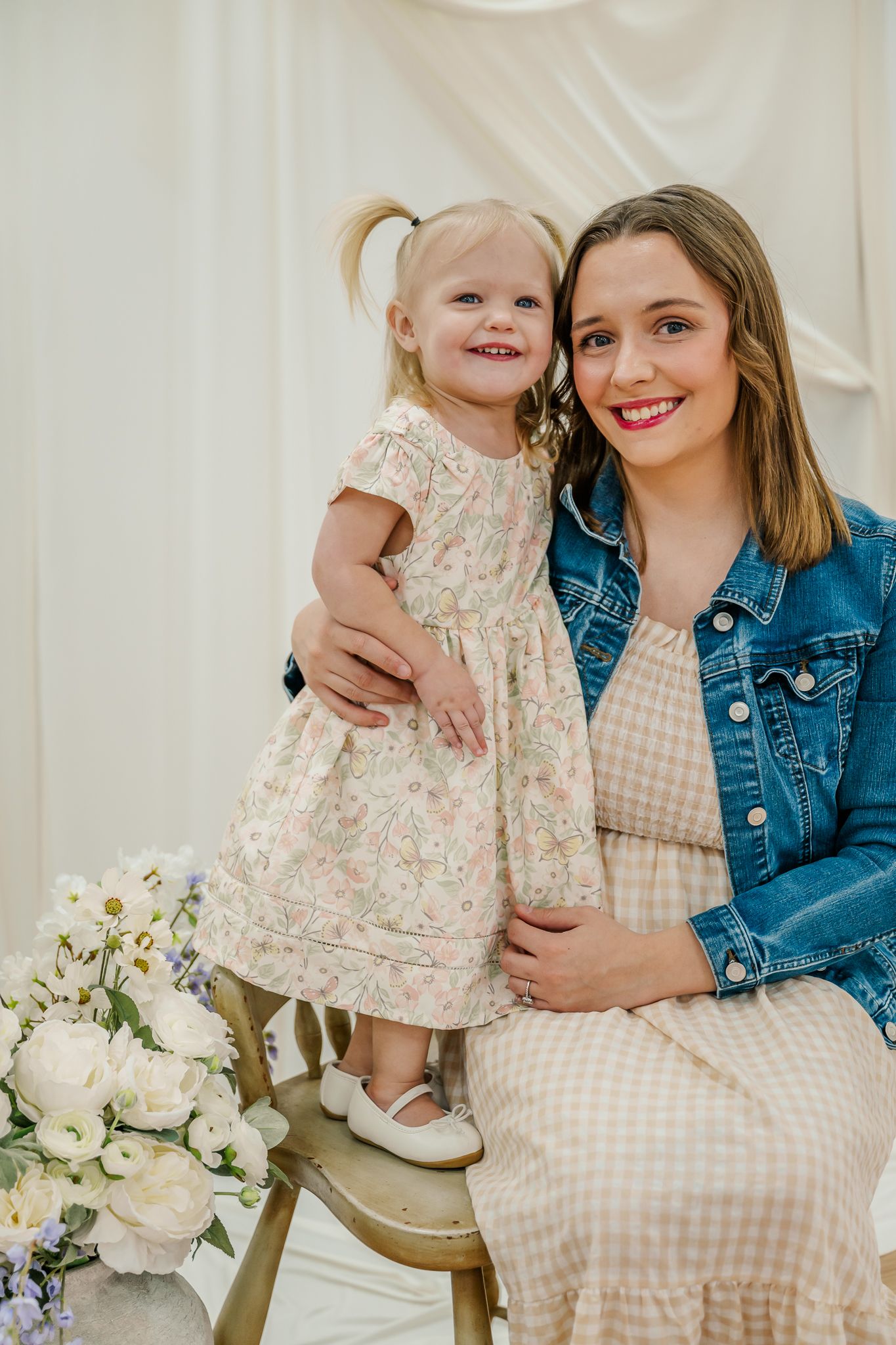 Sweet family moments captured against white backdrop with floral arrangements and coordinated spring dresses.