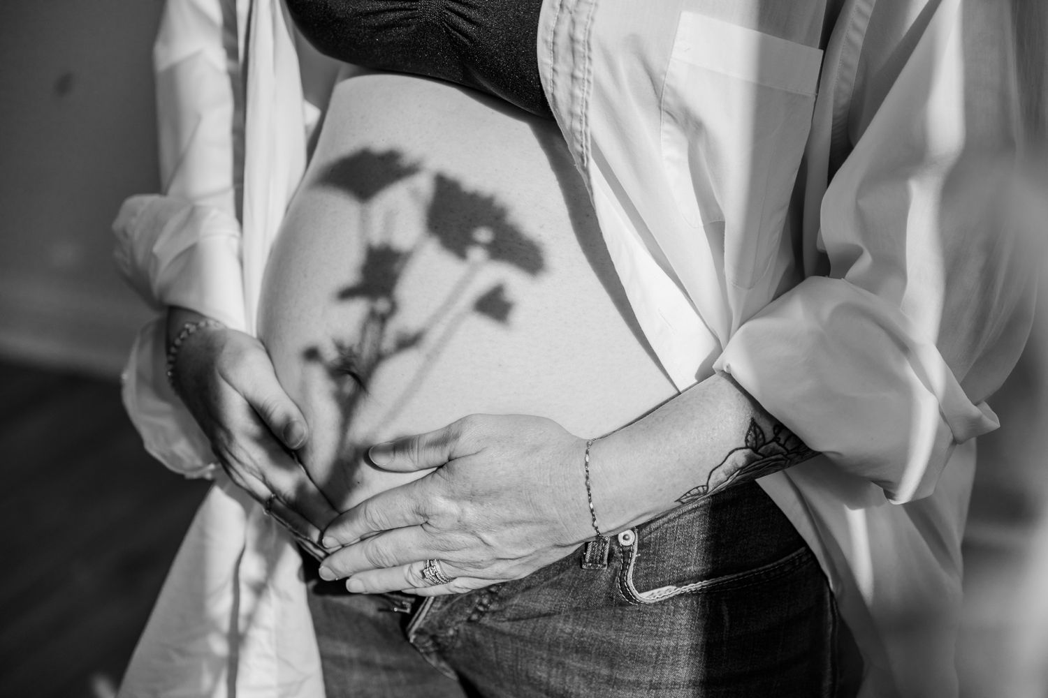 Black and white maternity photo of pregnant woman cradling baby bump with flower shadow cast on skin. Willow & Oaks Studios.