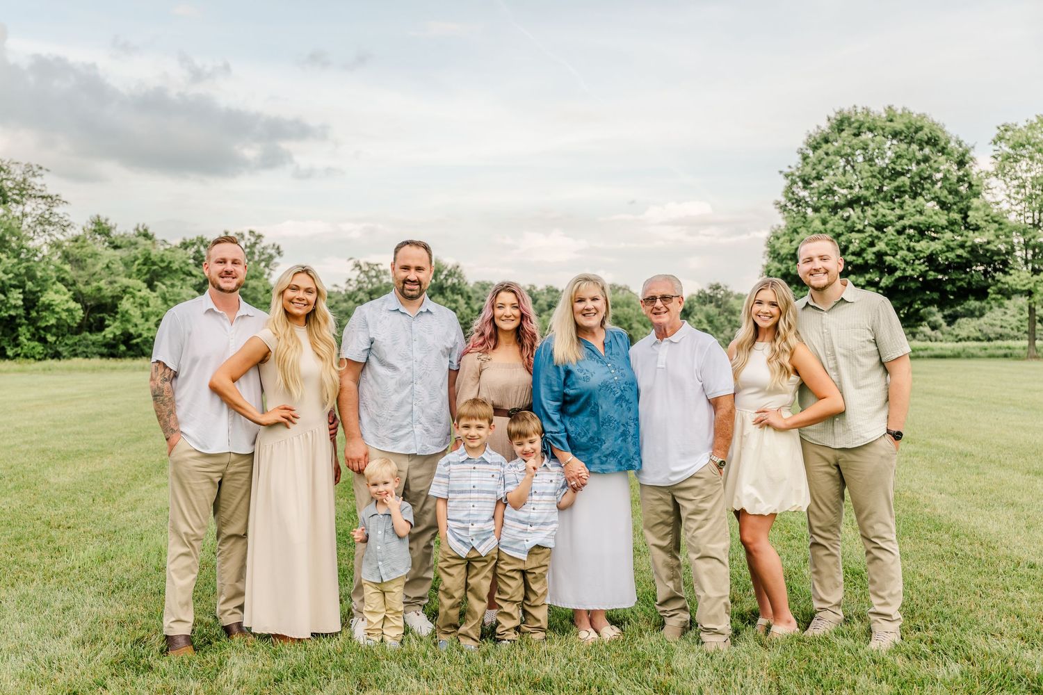 Wedding party in neutral tones posing together on grassy lawn.