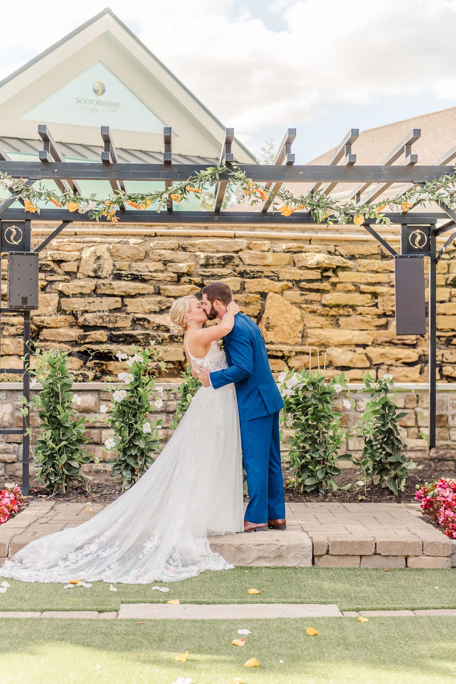 Couple shares their first kiss under a stone pergola during outdoor wedding ceremony.