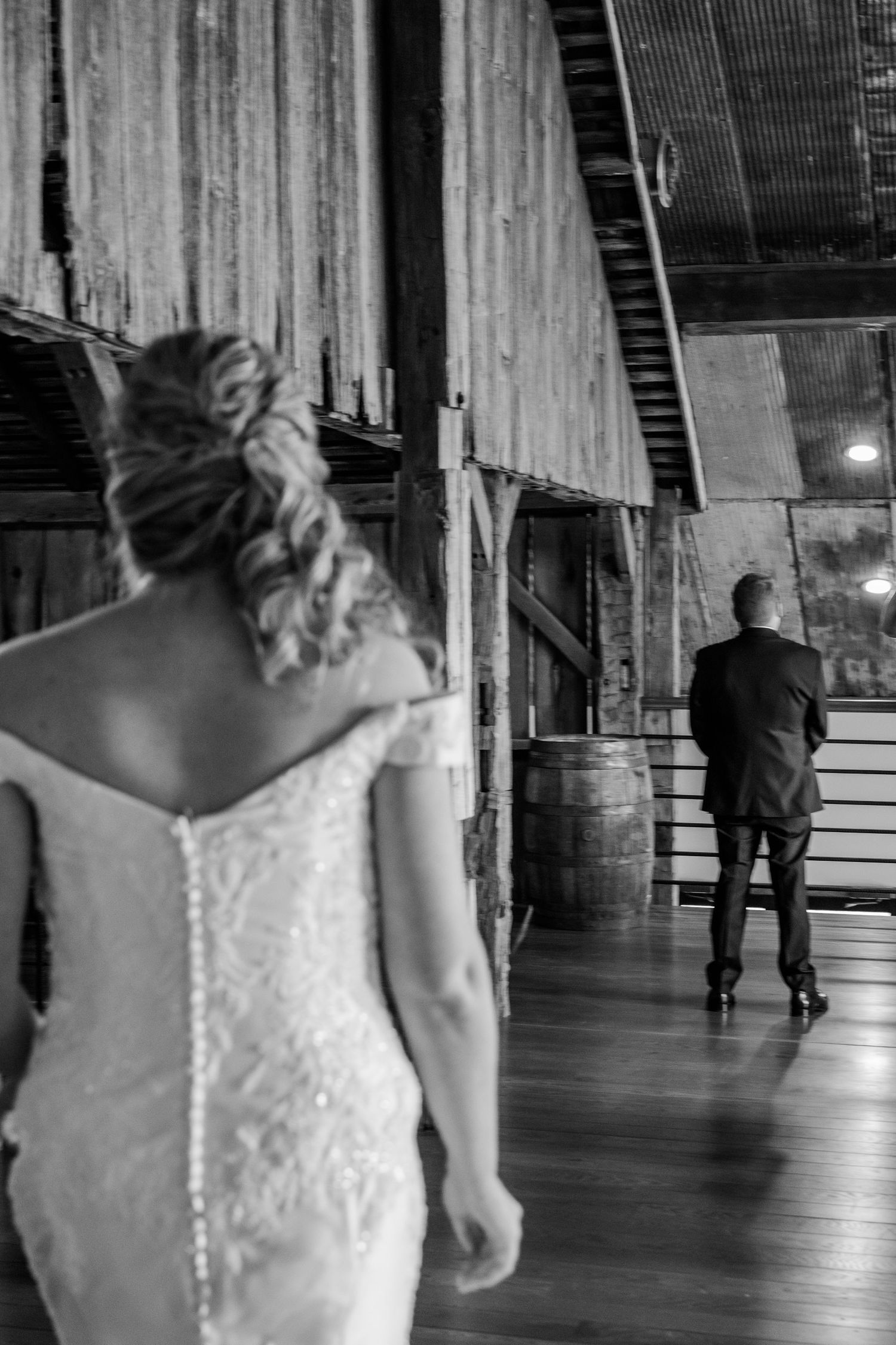 A bride in a lace-backed wedding dress walks through a rustic wooden venue. The Old Barns at Dry Run Farms in Williamsport, OH.