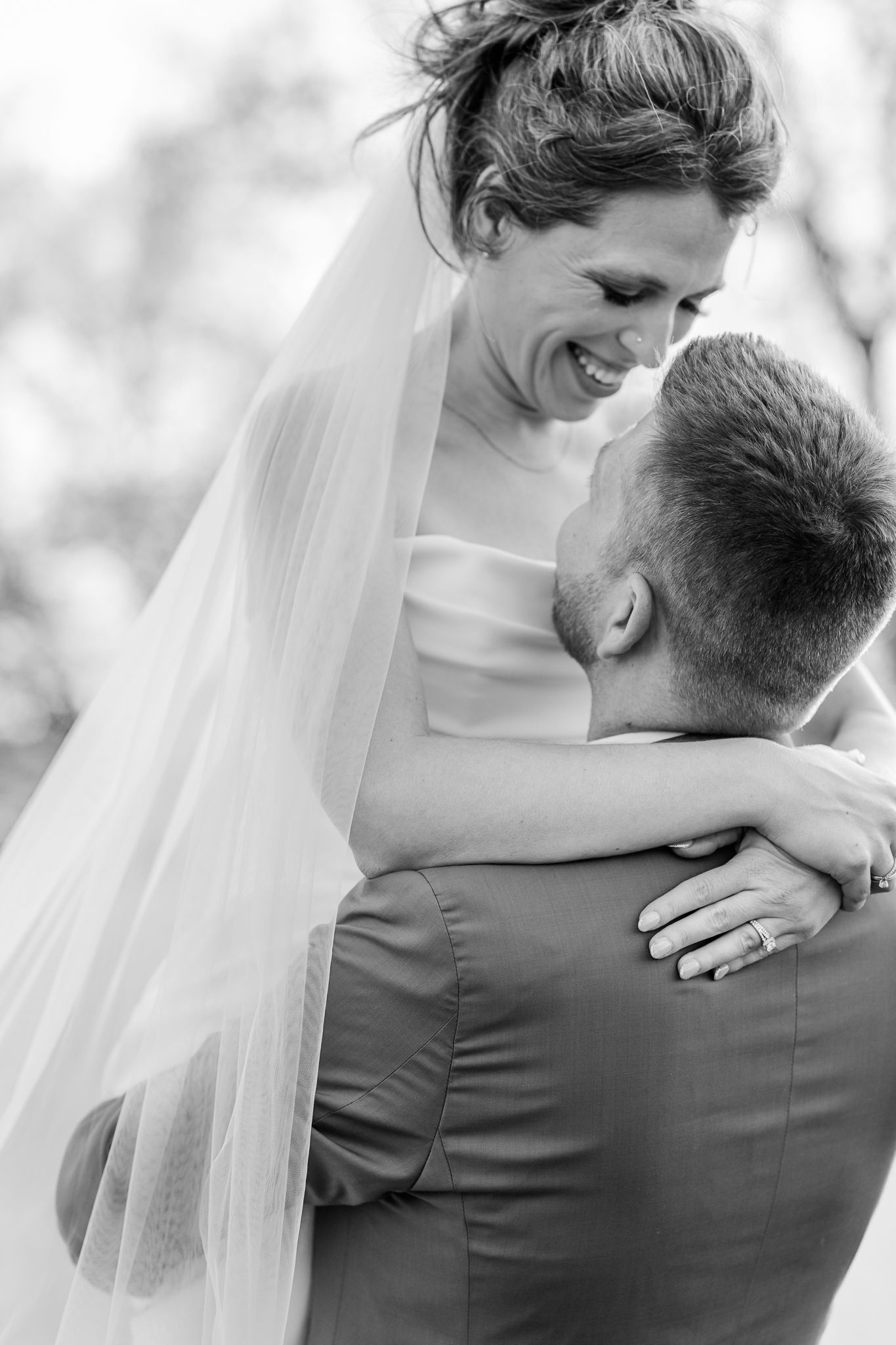 Black & white photo of groom lifting bride as she laughs and wraps her arms around his neck. The Old Barns at Dry Run Farms in Williamsport.