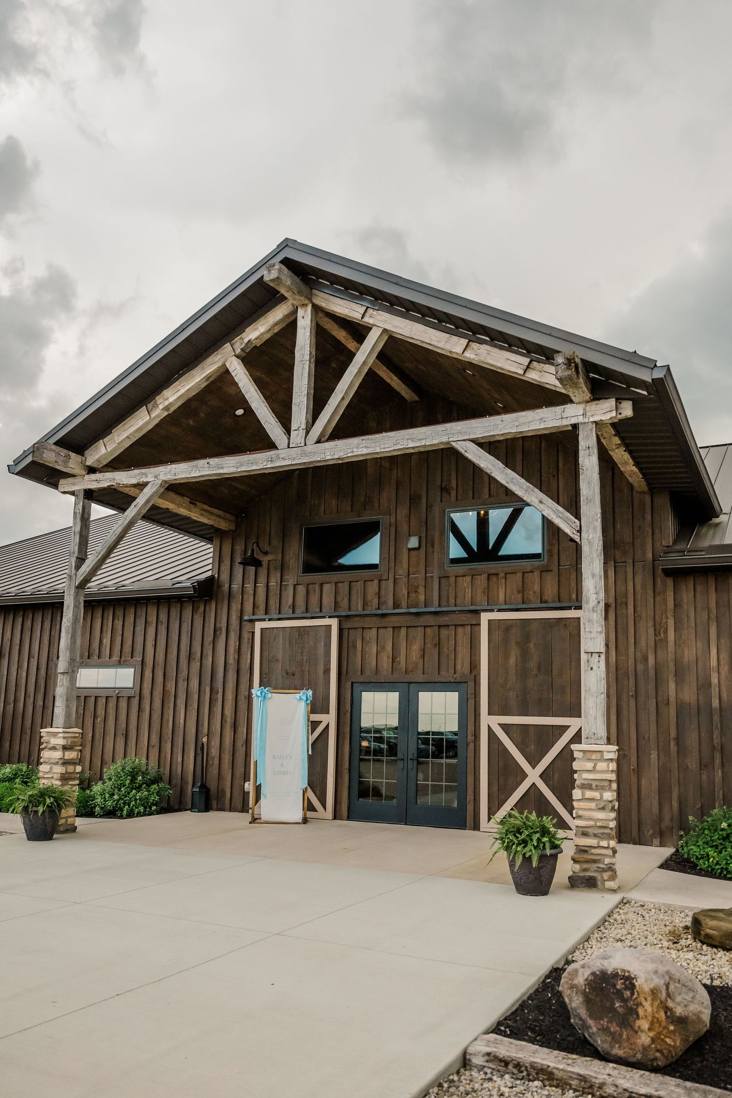 Rustic barn-style wedding venue exterior with wooden beams and stone accents under cloudy skies.The Old Barns at Dry Run Farms in Williamspo