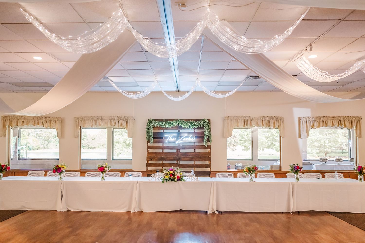 Elegant wedding reception venue with white draped ceiling, string lights, and tables set up for a celebration.