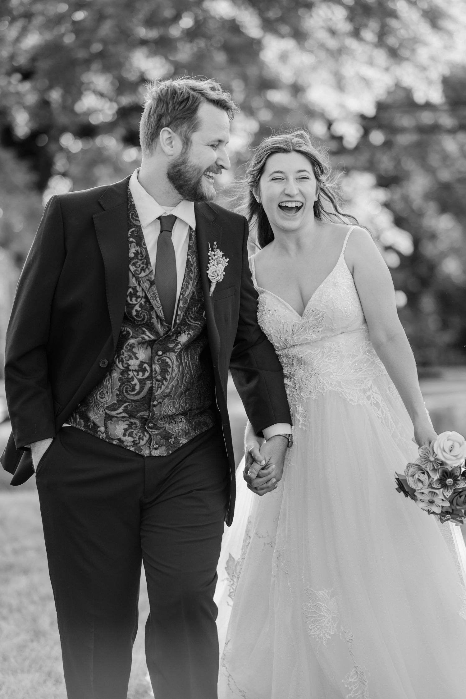 Joyful newlyweds laugh while walking together outdoors in black and white photography.