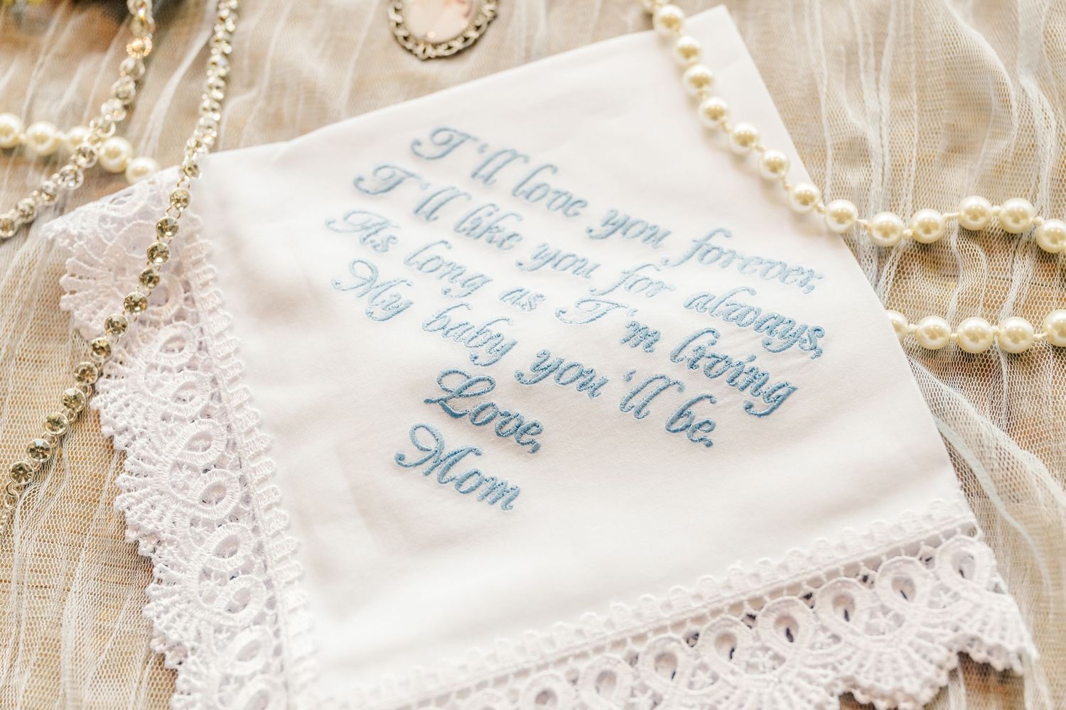 Delicate white handkerchiefs with blue embroidered text and lace trim displayed on a light fabric background.