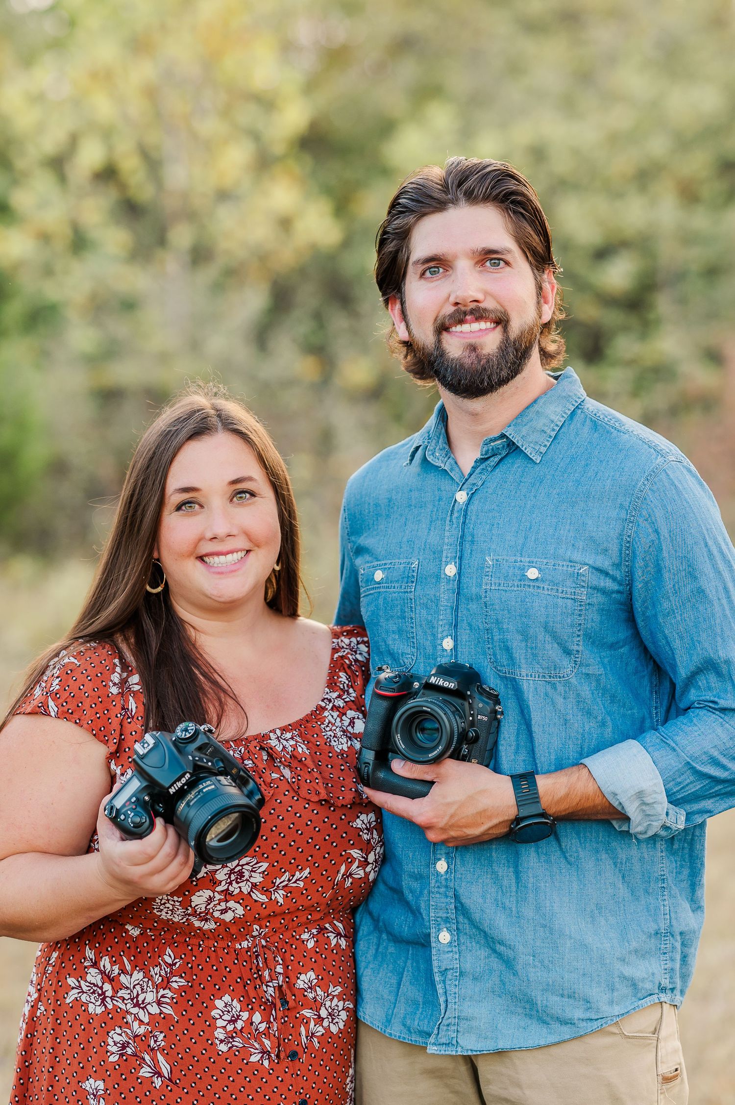 Photography duo with cameras posing outdoors in casual attire.
