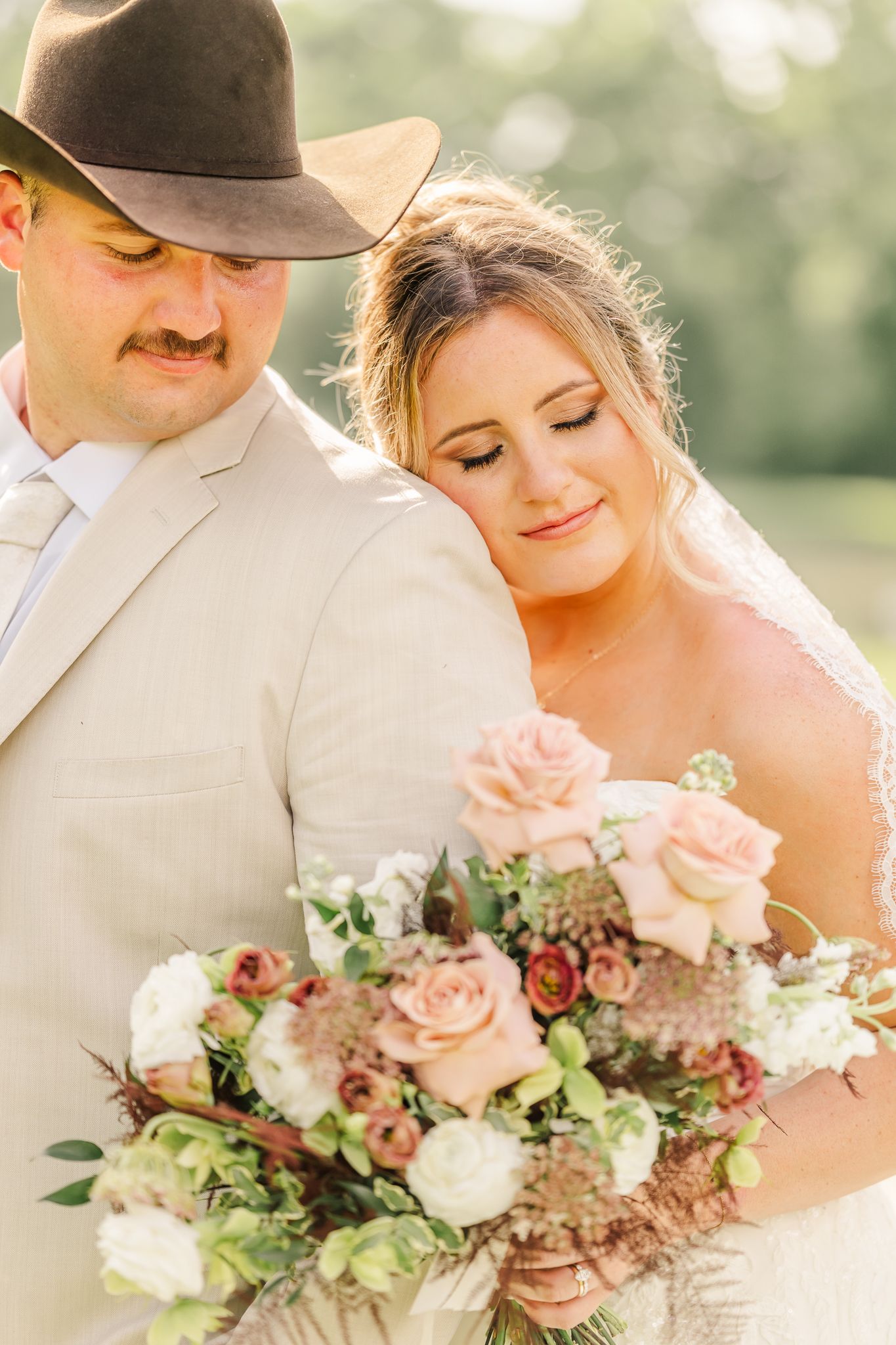 Bride and groom holding a blush pink and white floral bouquet, groom wearing a tan suit and cowboy hat. Canopy Creek Farm wedding venue