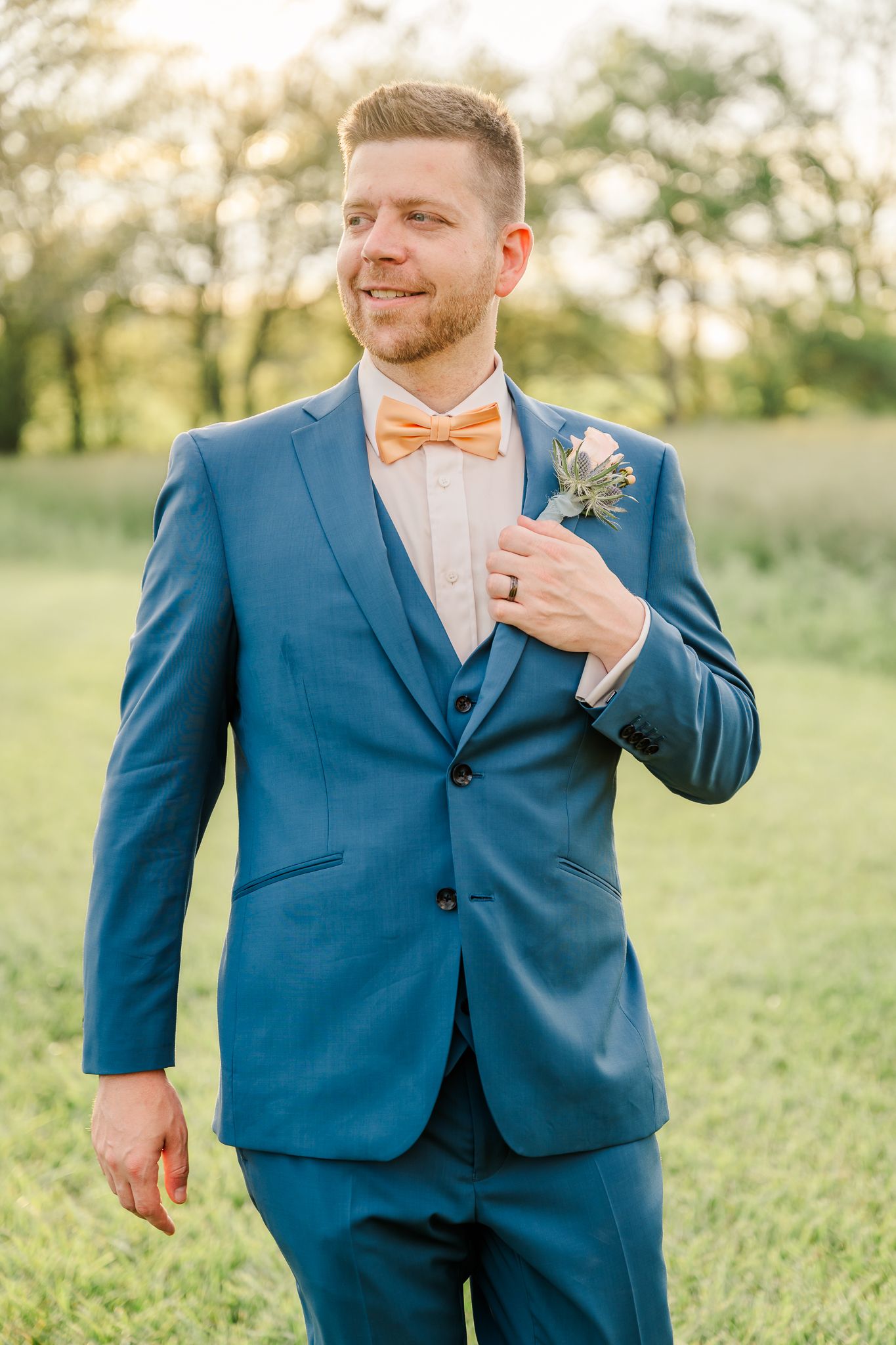 Groom in blue suit and peach bow tie smiling outdoors in golden hour sunlight.The Old Barns at Dry Run Farms in Williamsport, Ohio.