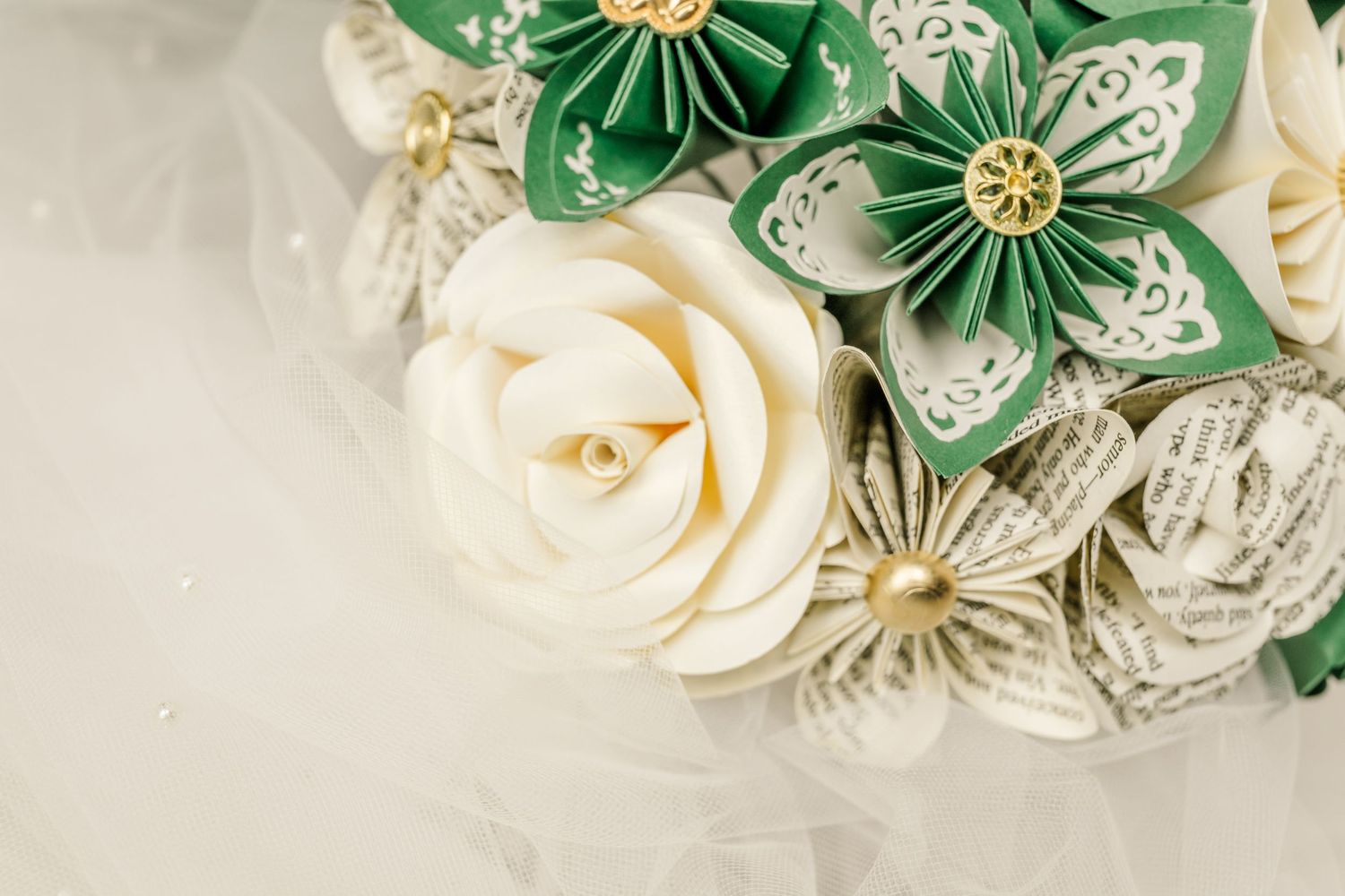 Handmade paper flowers in emerald green and ivory white with vintage book page accents create an elegant arrangement.