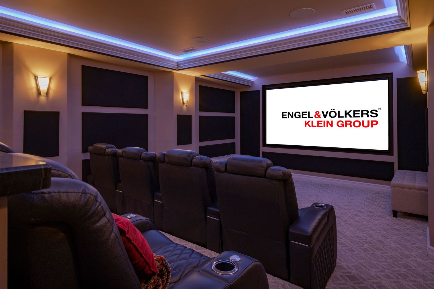 Luxurious home theater room with leather recliners, ambient lighting, and large Engel & Volkers Klein Group projection screen.