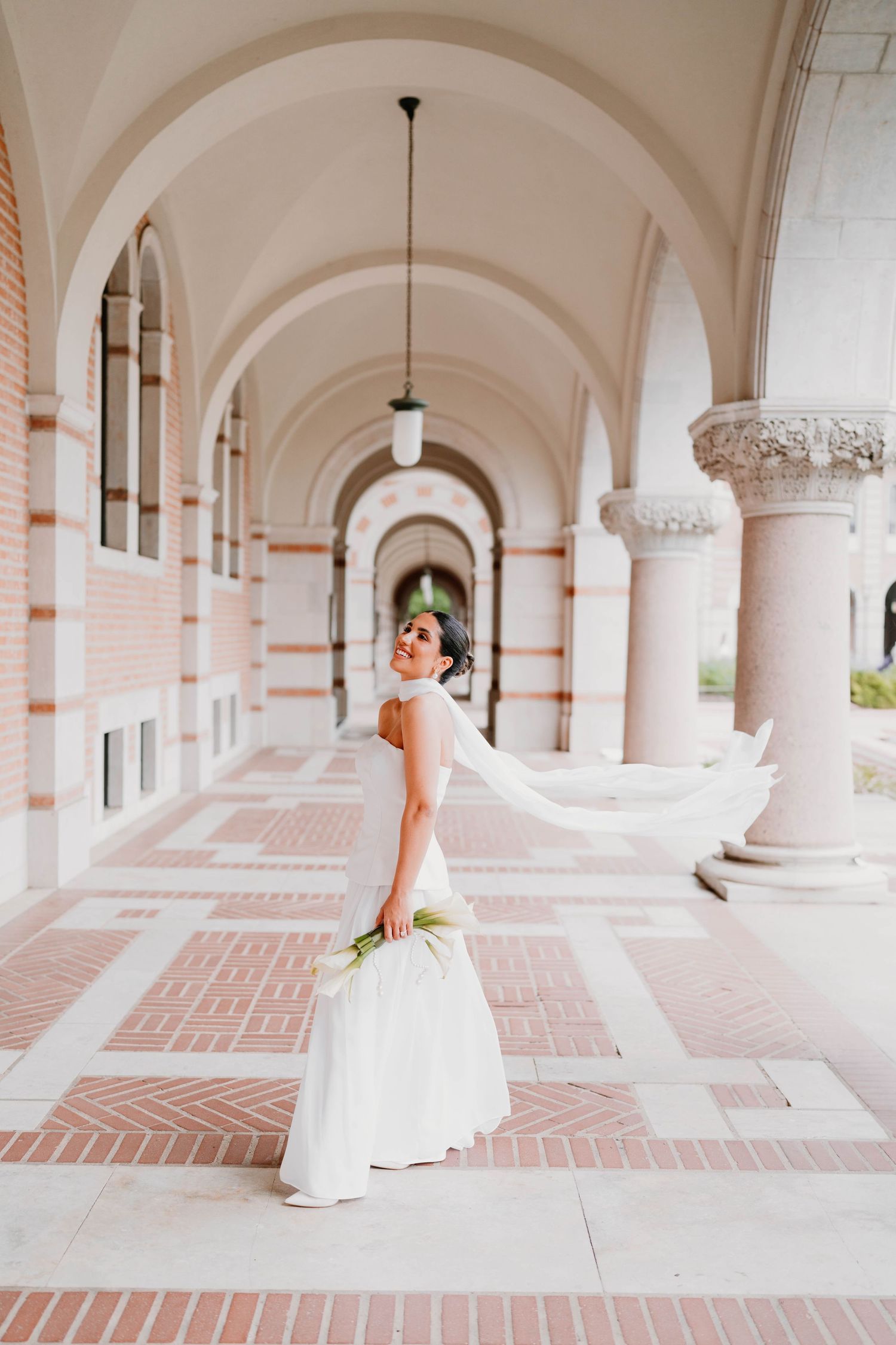 Bride twirls her dress in a stunning architectural corridor with arched columns.