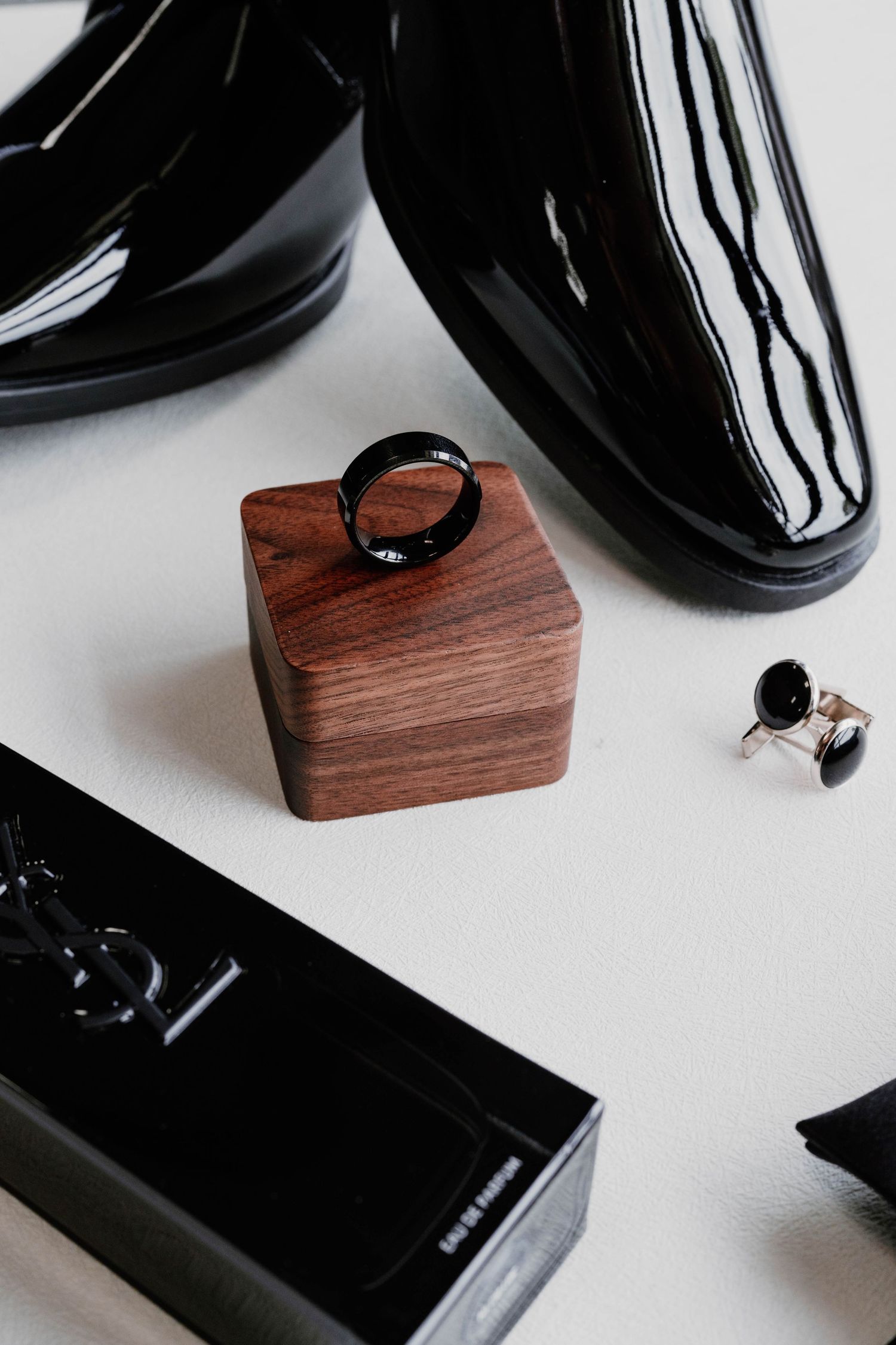 Black dress shoes and wedding rings displayed on wooden blocks against white background.