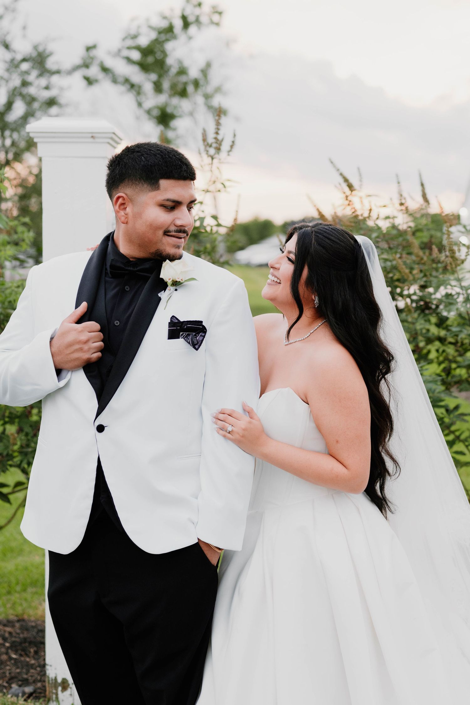 A joyful wedding couple in white and black formal attire share candid moments outdoors.