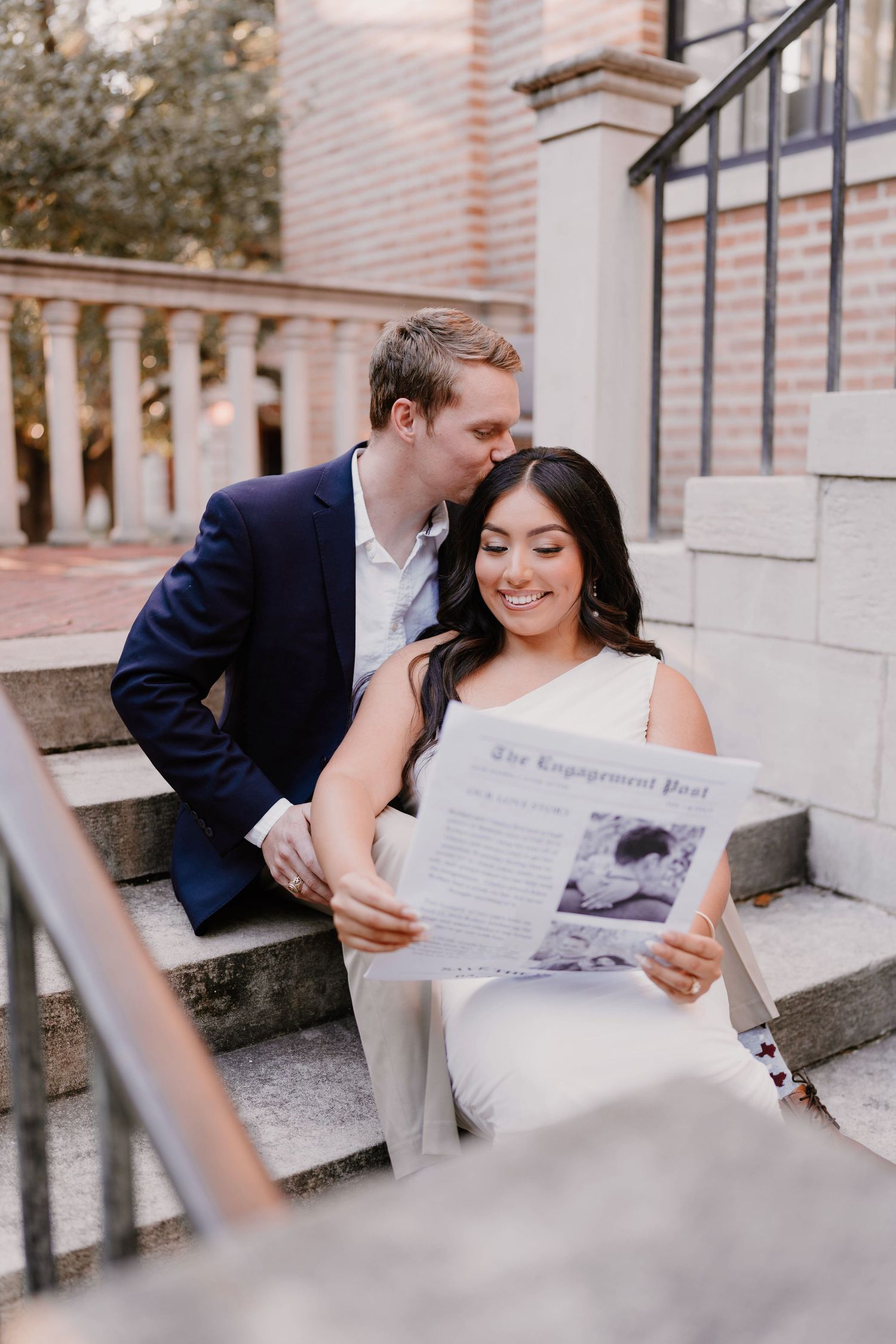 A couple shares an intimate moment on stone steps while reading a newspaper together.