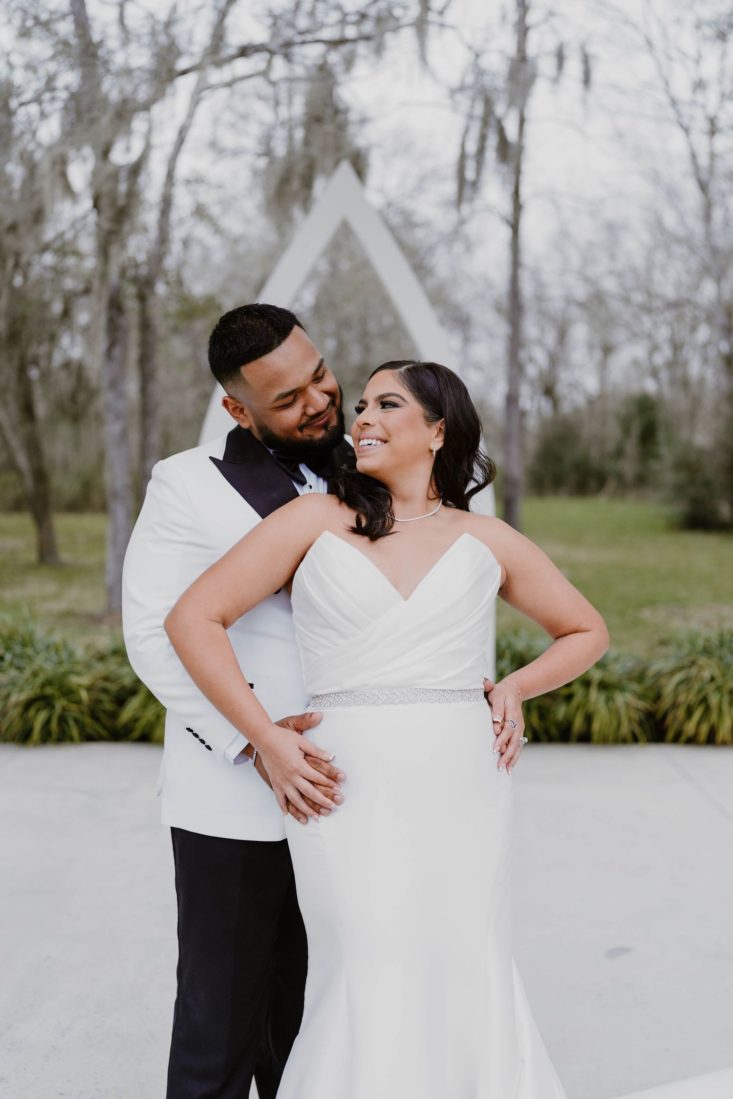 Romantic wedding couple shares intimate moments outdoors near a white pavilion.