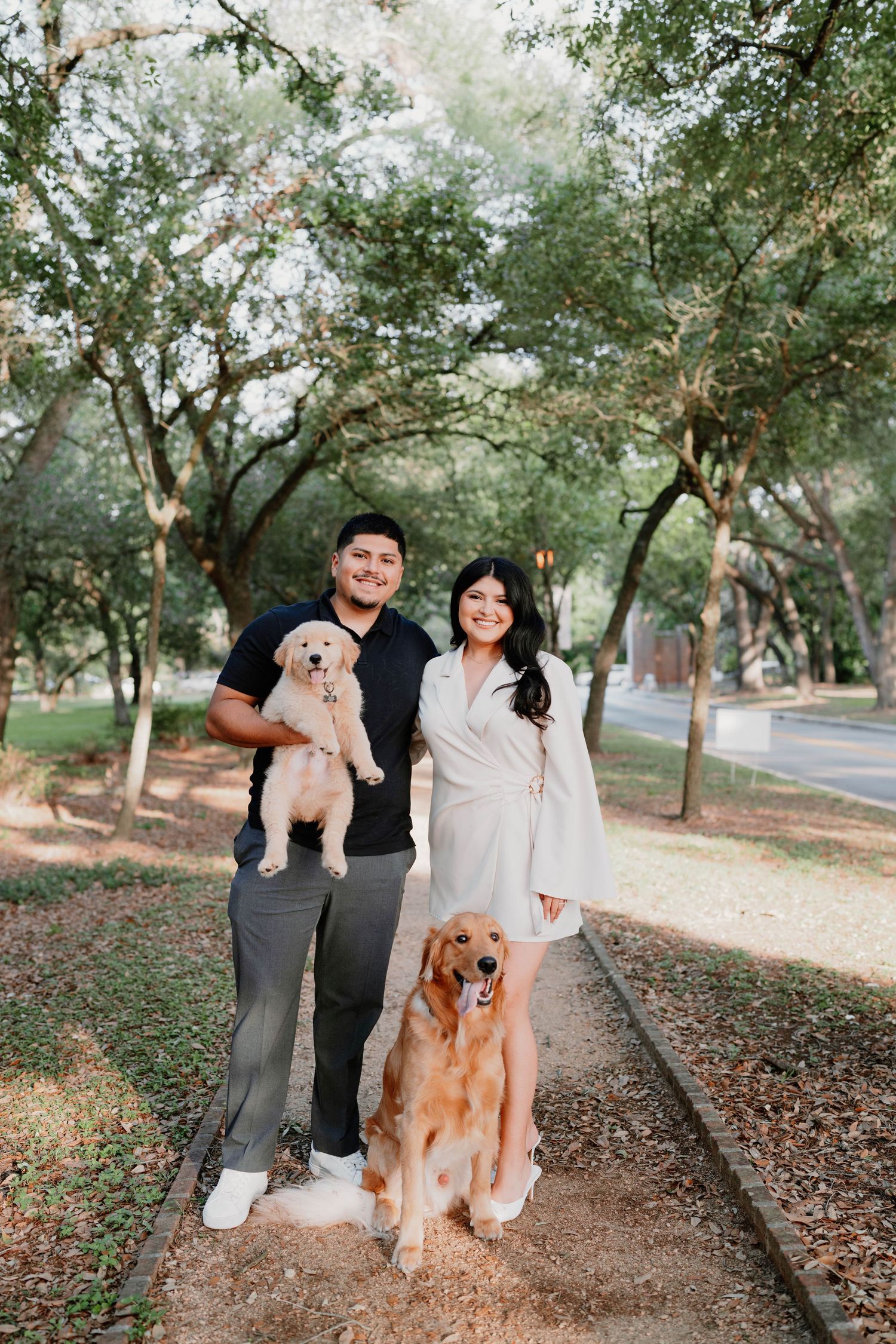 A couple and their dogs pose for family portraits in a wooded outdoor setting.