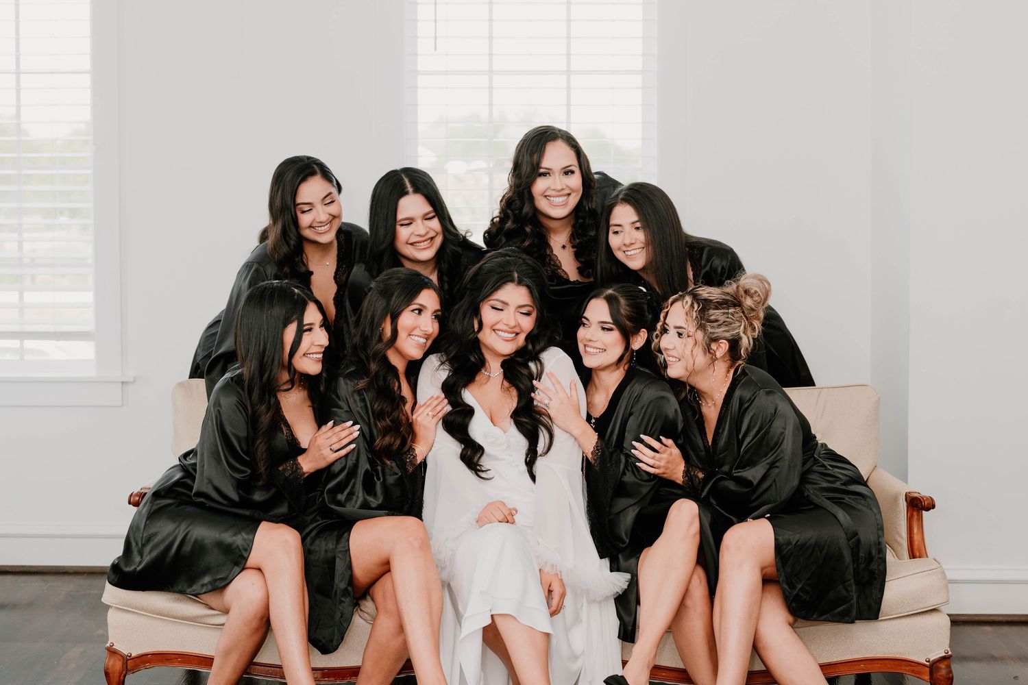 Group of bridesmaids in black robes sitting together and laughing on a couch.