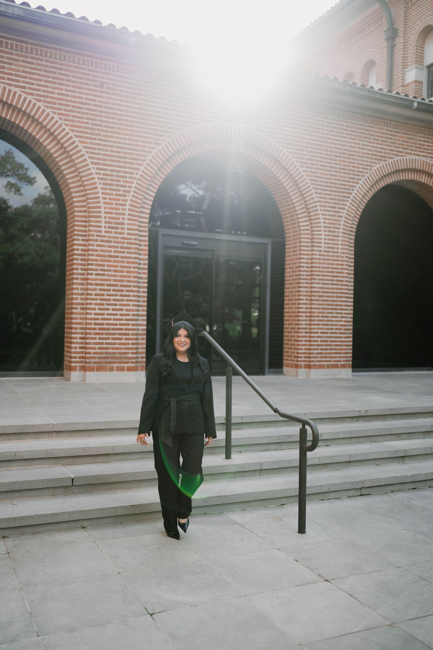 Graduate walking along brick archways in traditional black graduation attire.