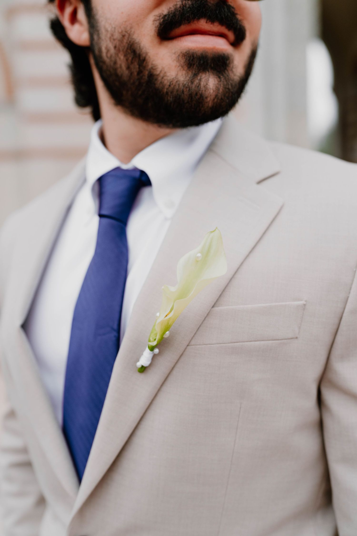 Close-up detail of groom's boutonniere and light beige suit with navy tie.