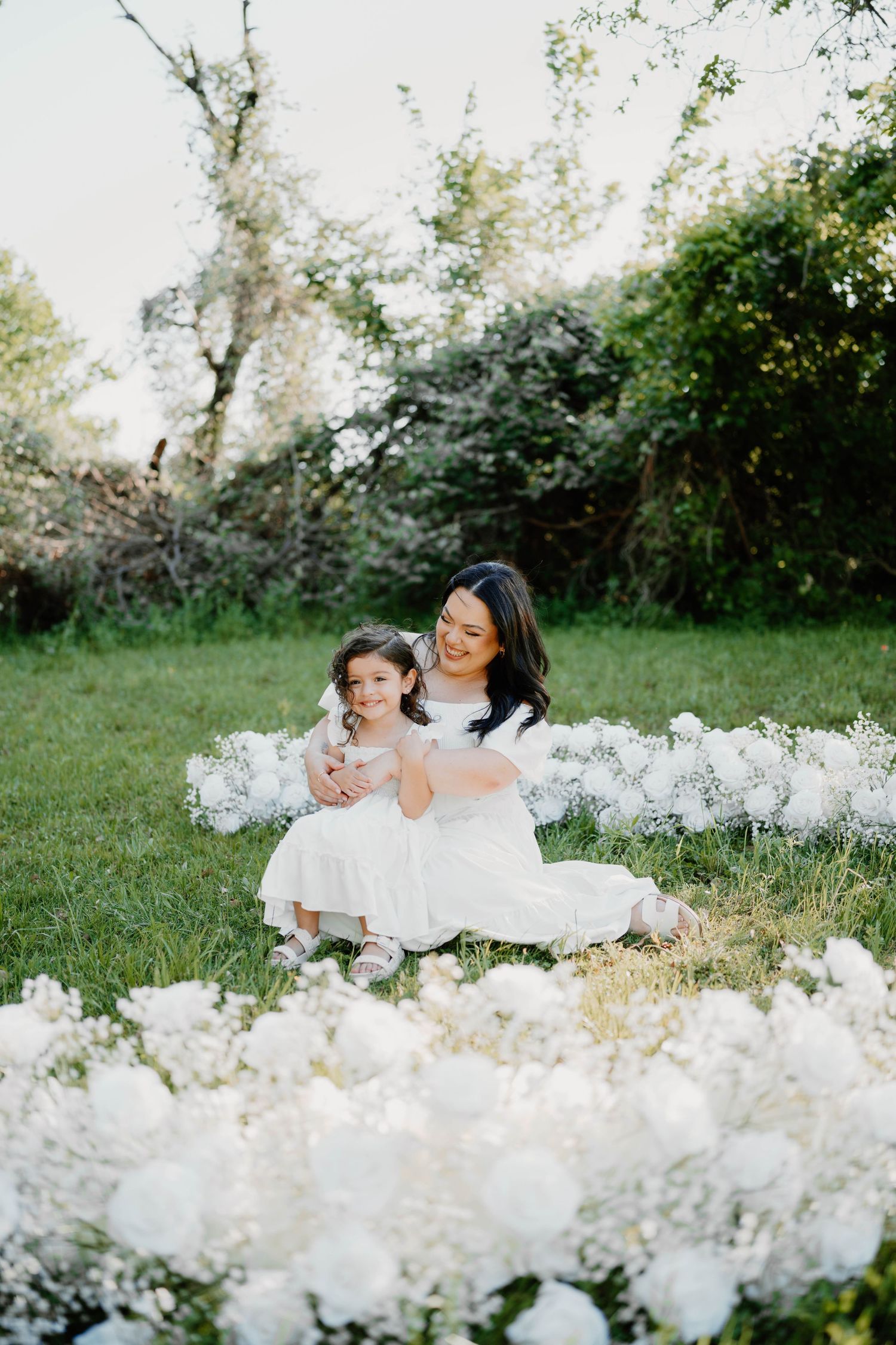 Mother and child lying among beautiful white flowers in a garden setting.