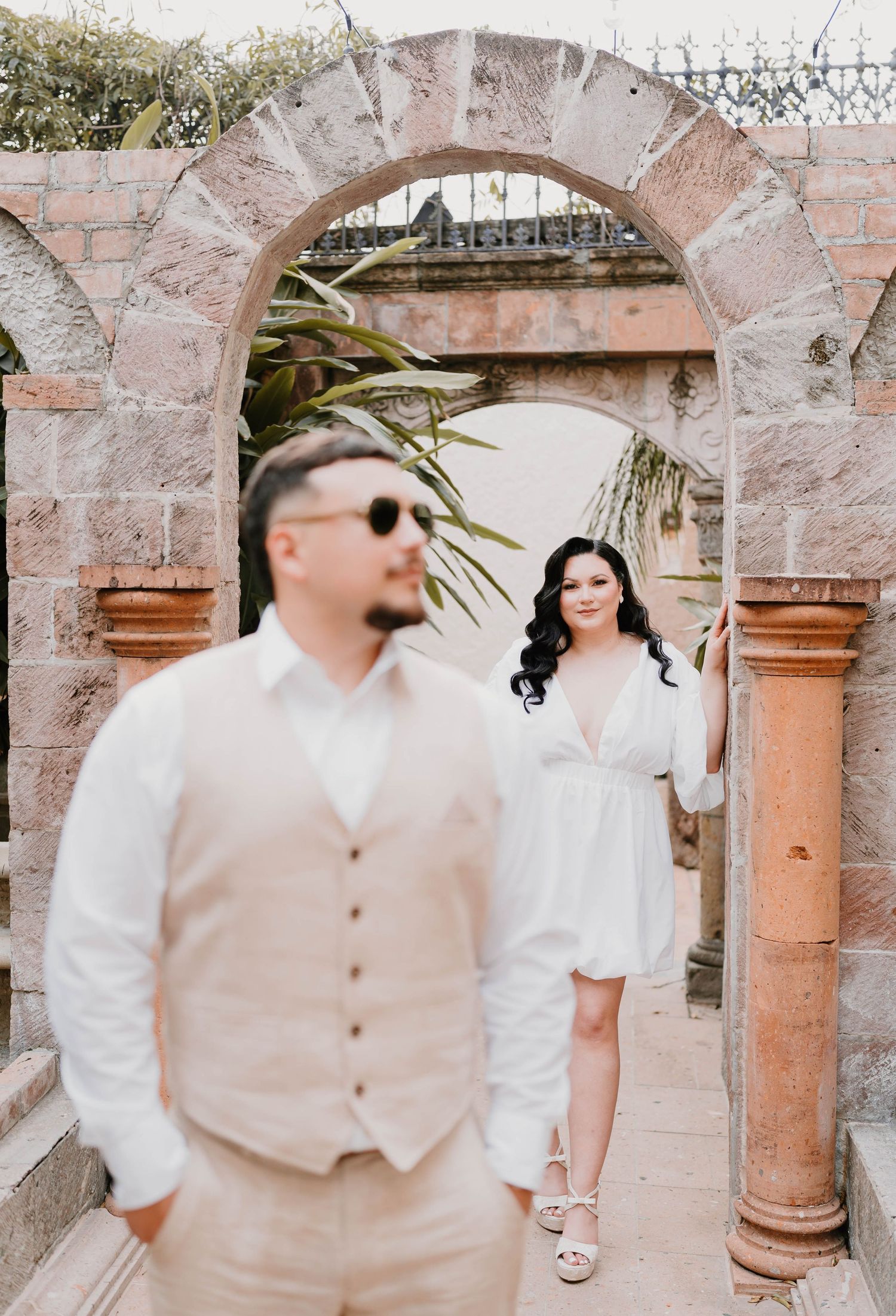 Romantic photoshoot sequence along a rustic stone archway with pink tones.