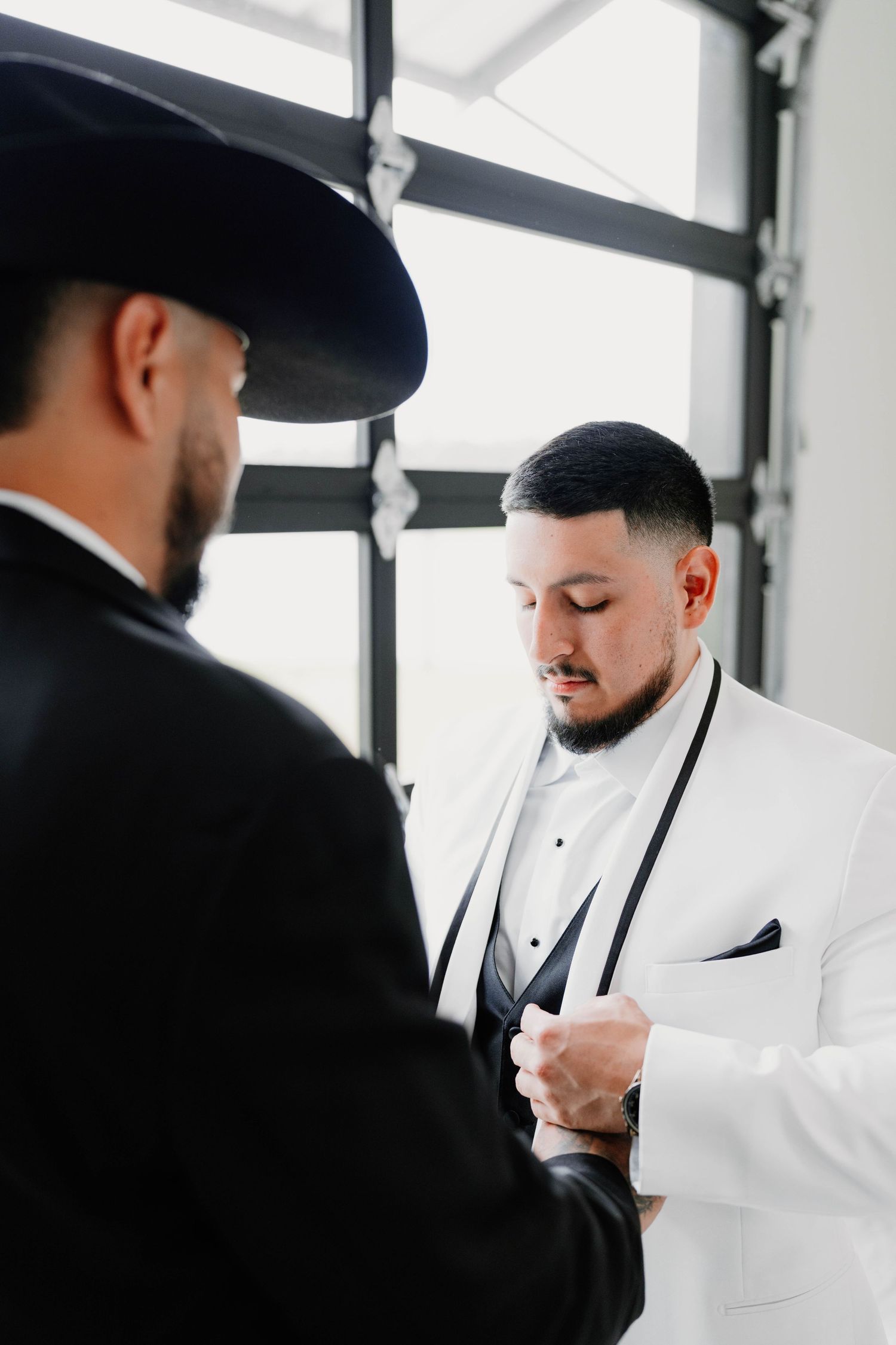 Groom in white tuxedo and black bow tie adjusts his cuffs before the ceremony.