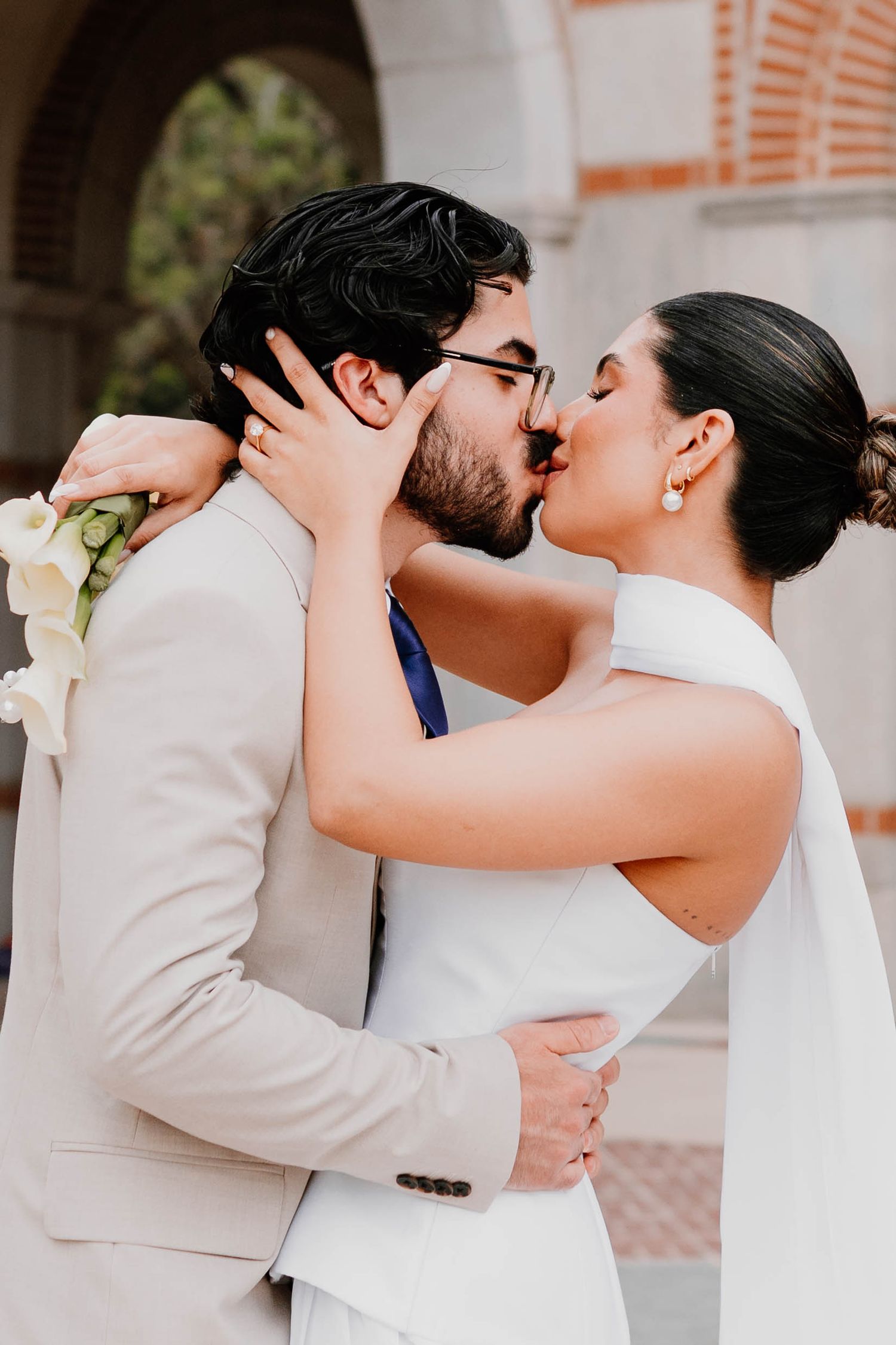 Romantic embrace between newlyweds against classical architecture background.