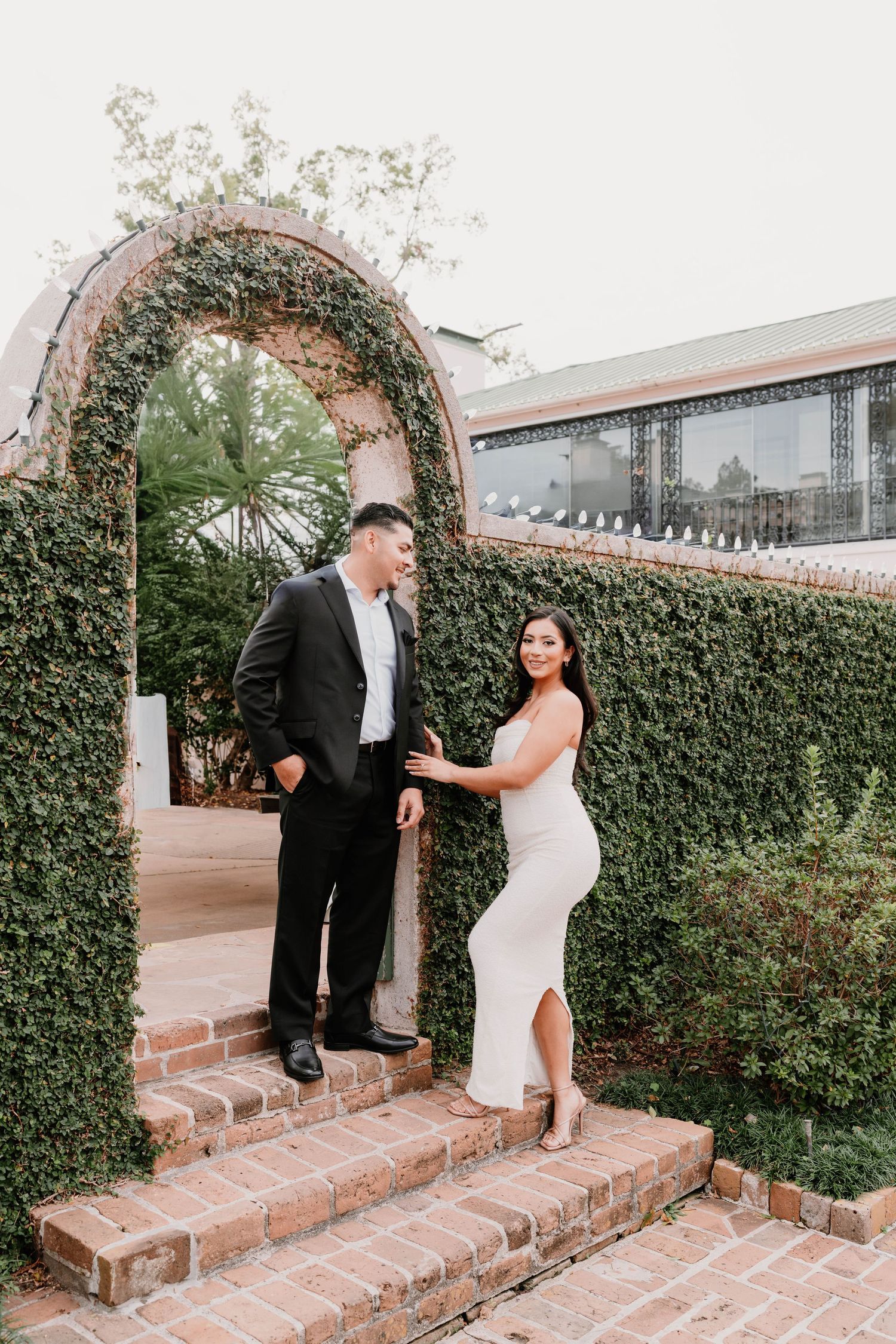 Pair stands in archway framed by green ivy and brick steps.