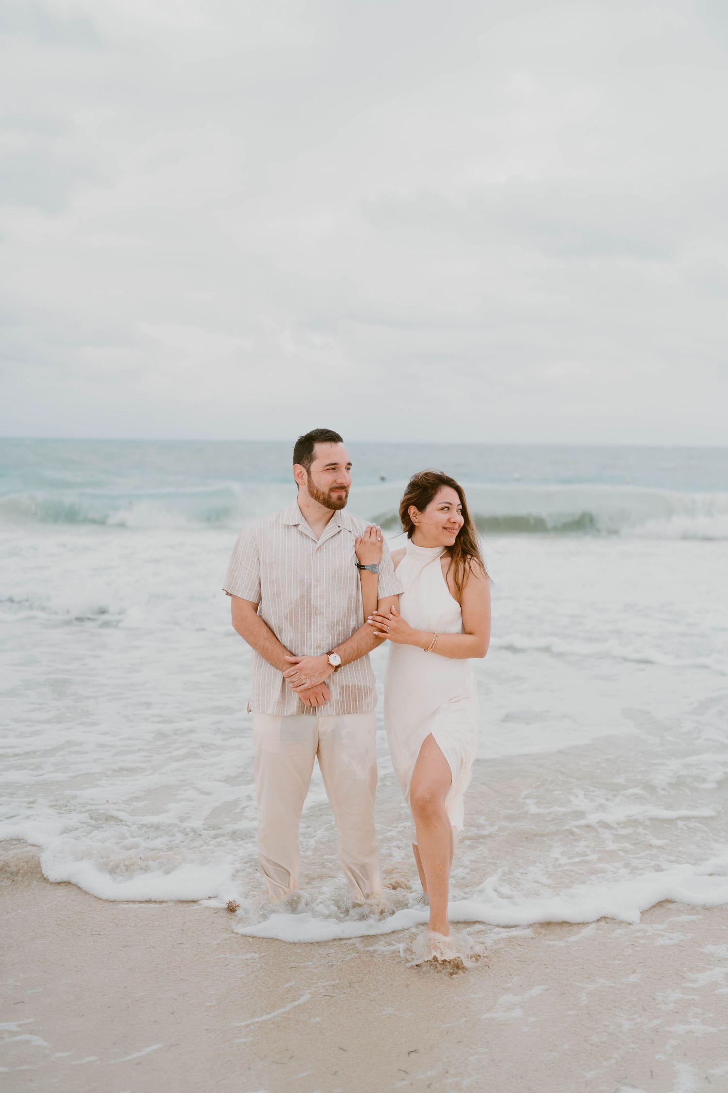 Playful couple splashes and laughs together in shallow ocean waves at beach.