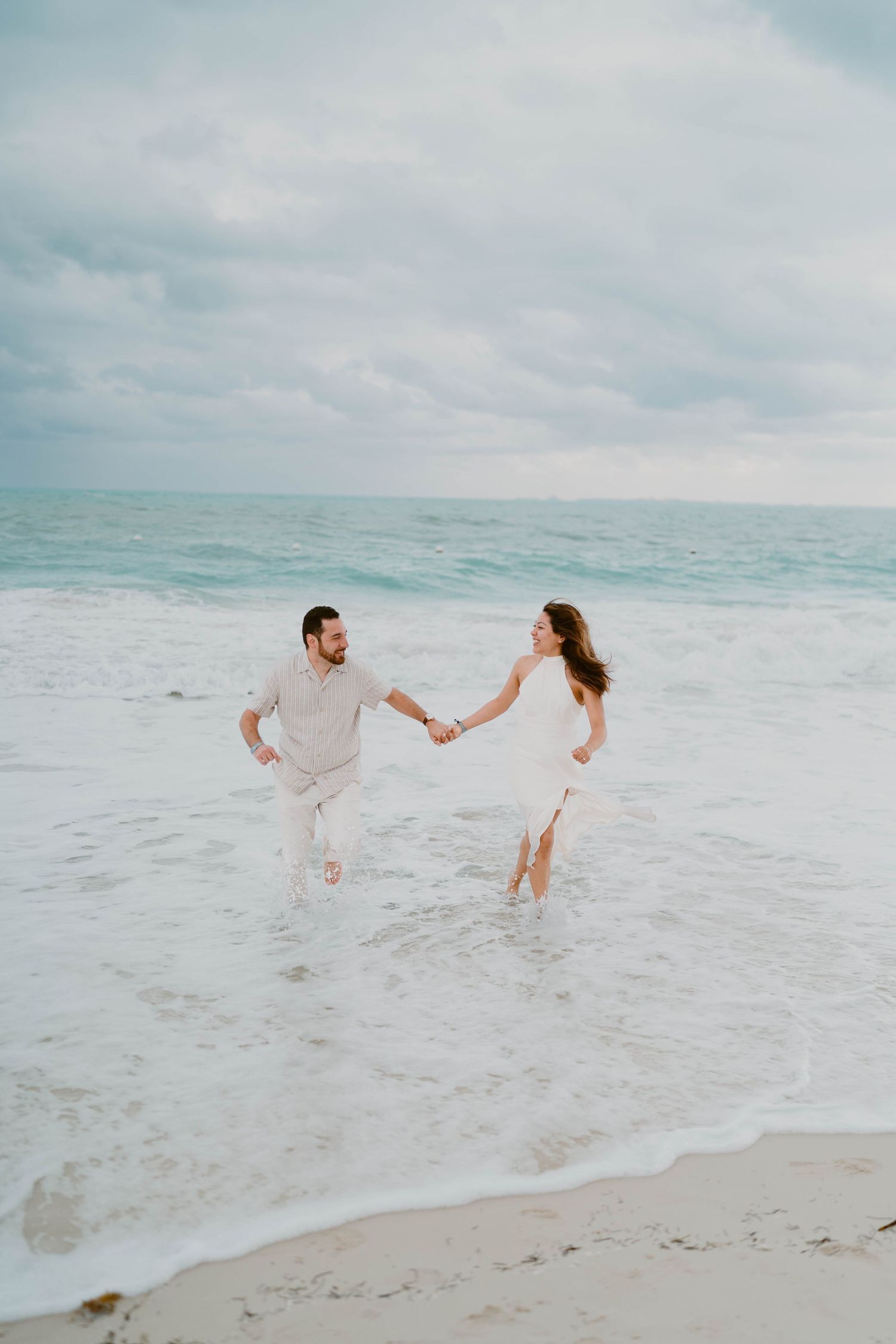 Couple runs and plays together along a serene beach with waves crashing in the background.