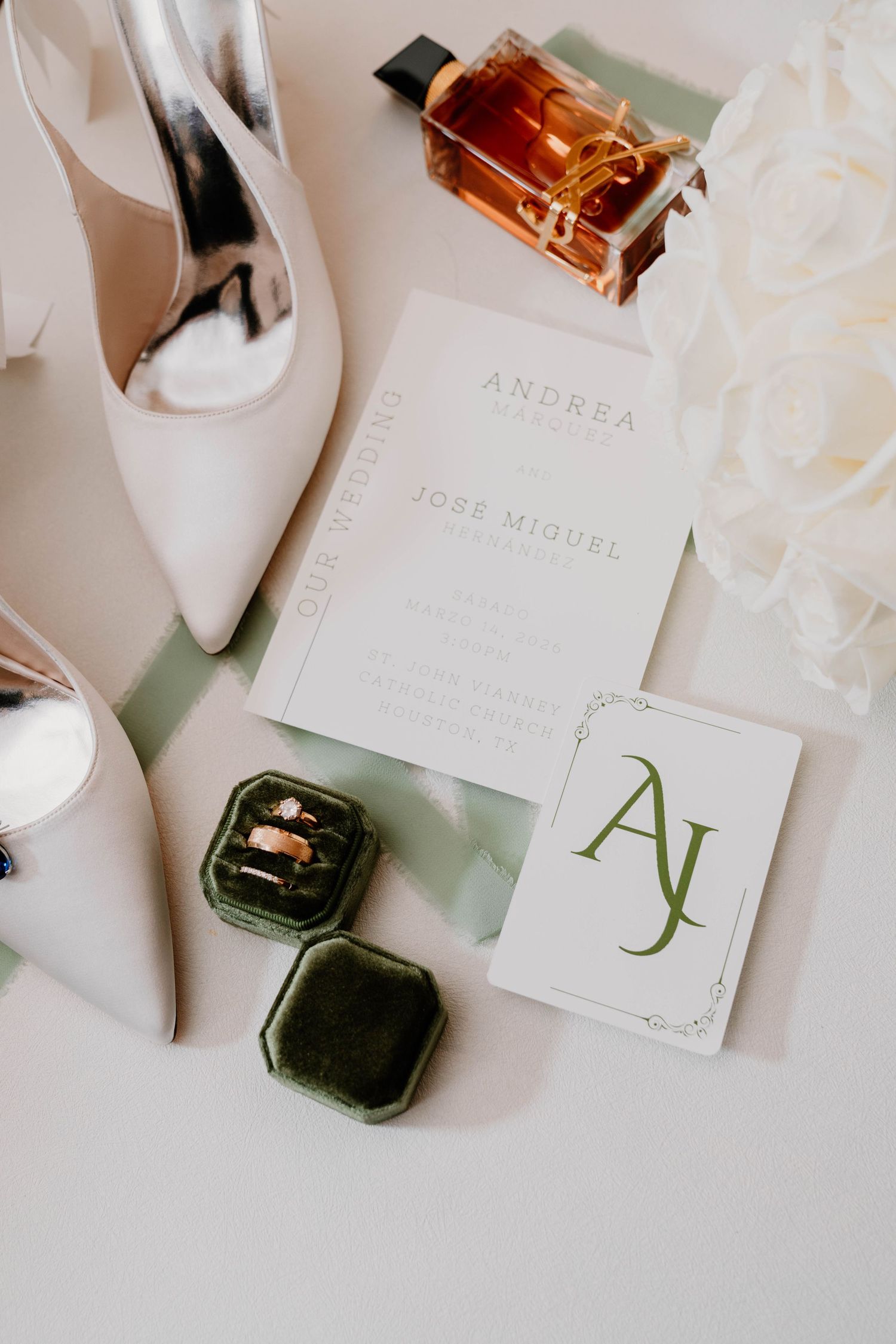 Wedding flat lay with white heels, rings in velvet box, invitation for Andrea and Jose Miguel, monogram card, and perfume bottle.