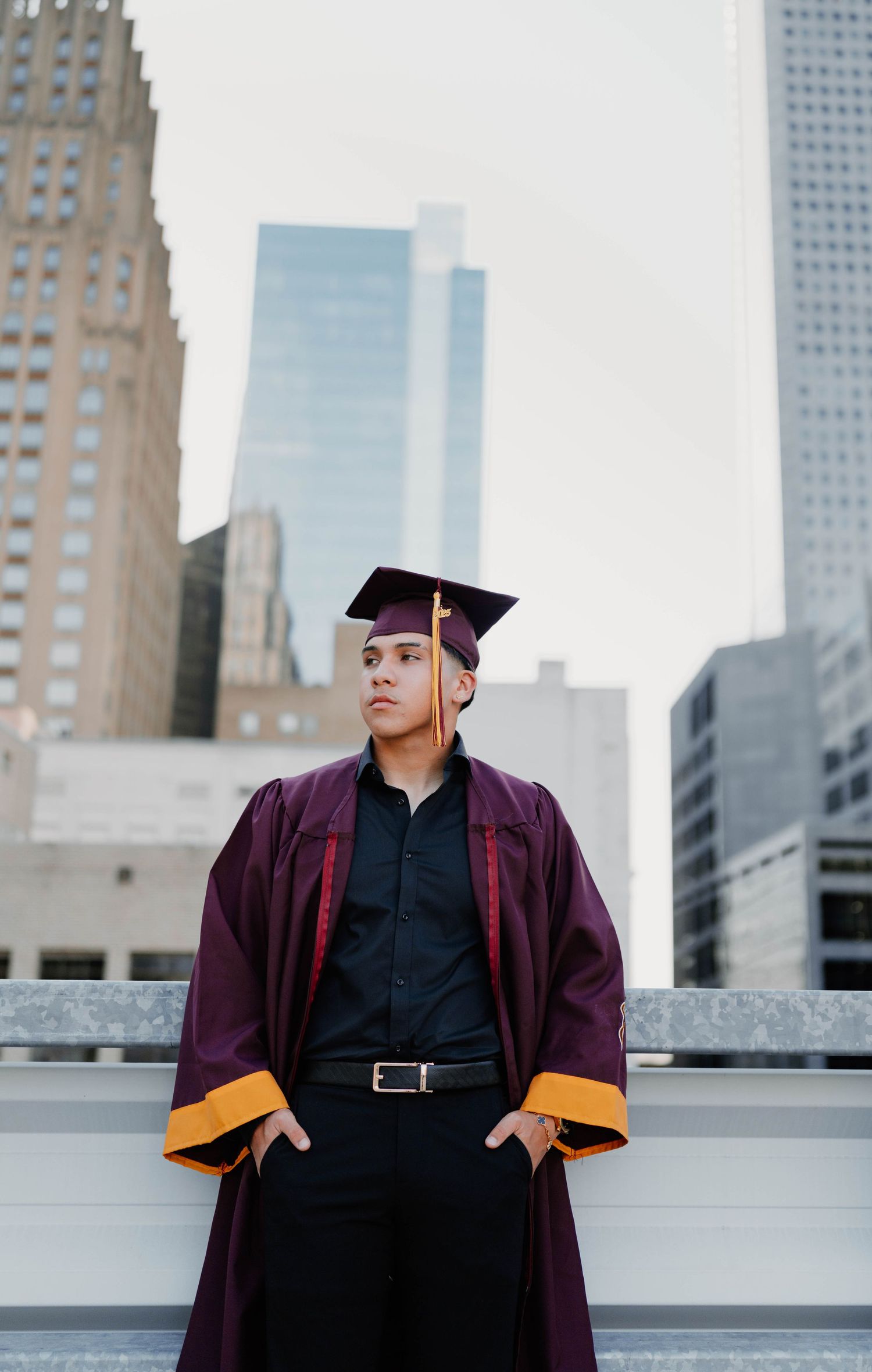 Graduation photoshoot on urban rooftop with maroon cap and gown against city skyline.