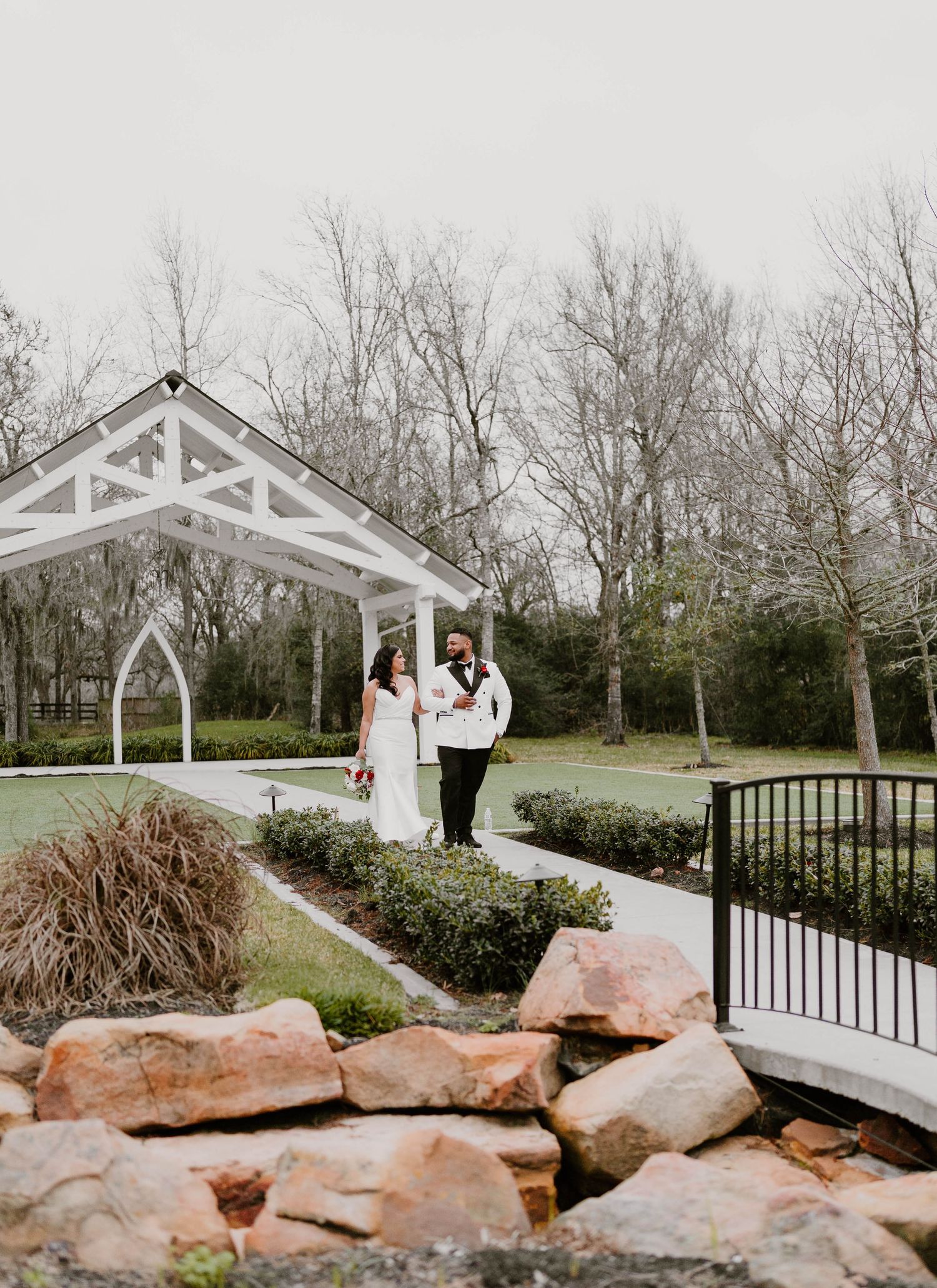 Wedding venue features white pavilion and natural stone landscaping surrounded by trees.