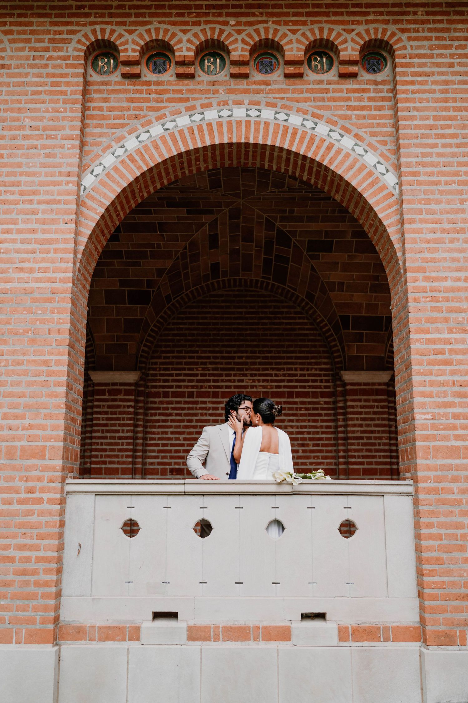Couple shares romantic moment on brick balcony of historic building.