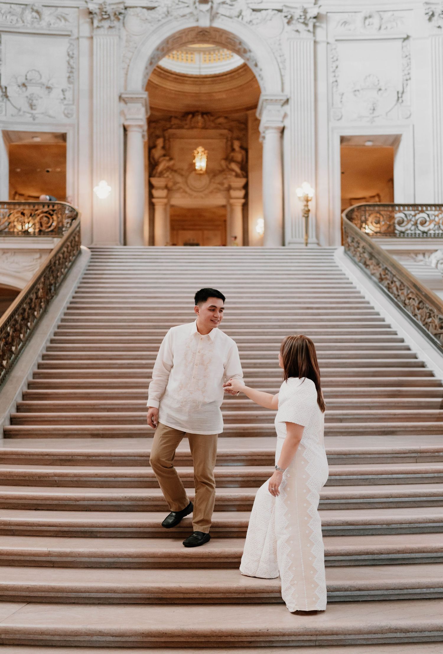 Couple in white outfits photographed on grand marble staircase sequence.
