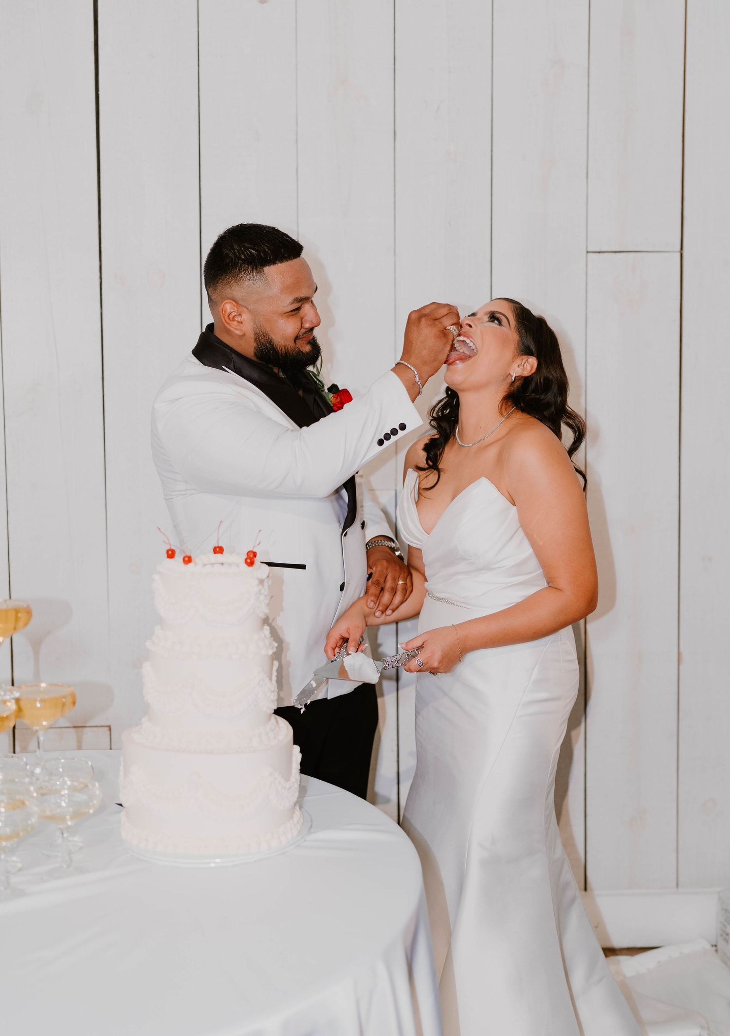 Wedding couple shares cake and champagne during reception in white barn venue.