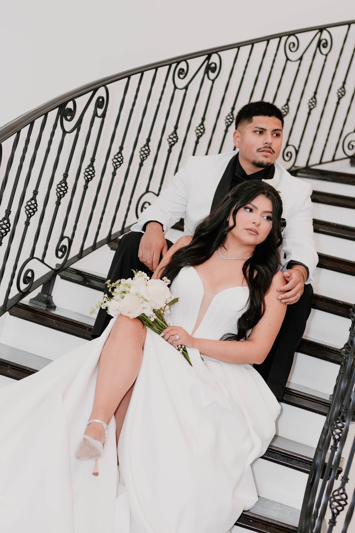 Wedding couple posing on elegant staircase with ornate iron railings.