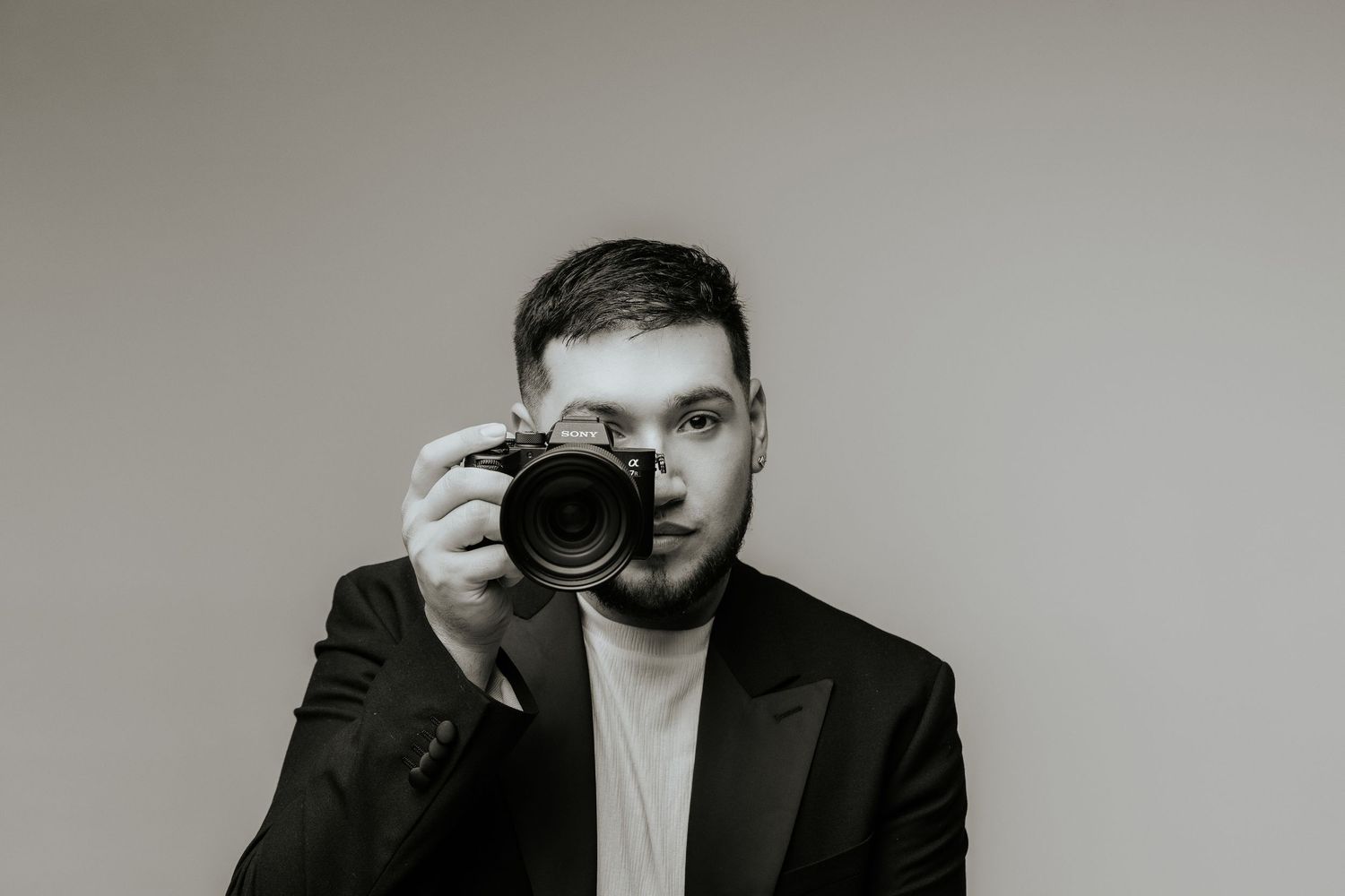A photographer in a black blazer holds up a professional camera to take a photo in black and white.