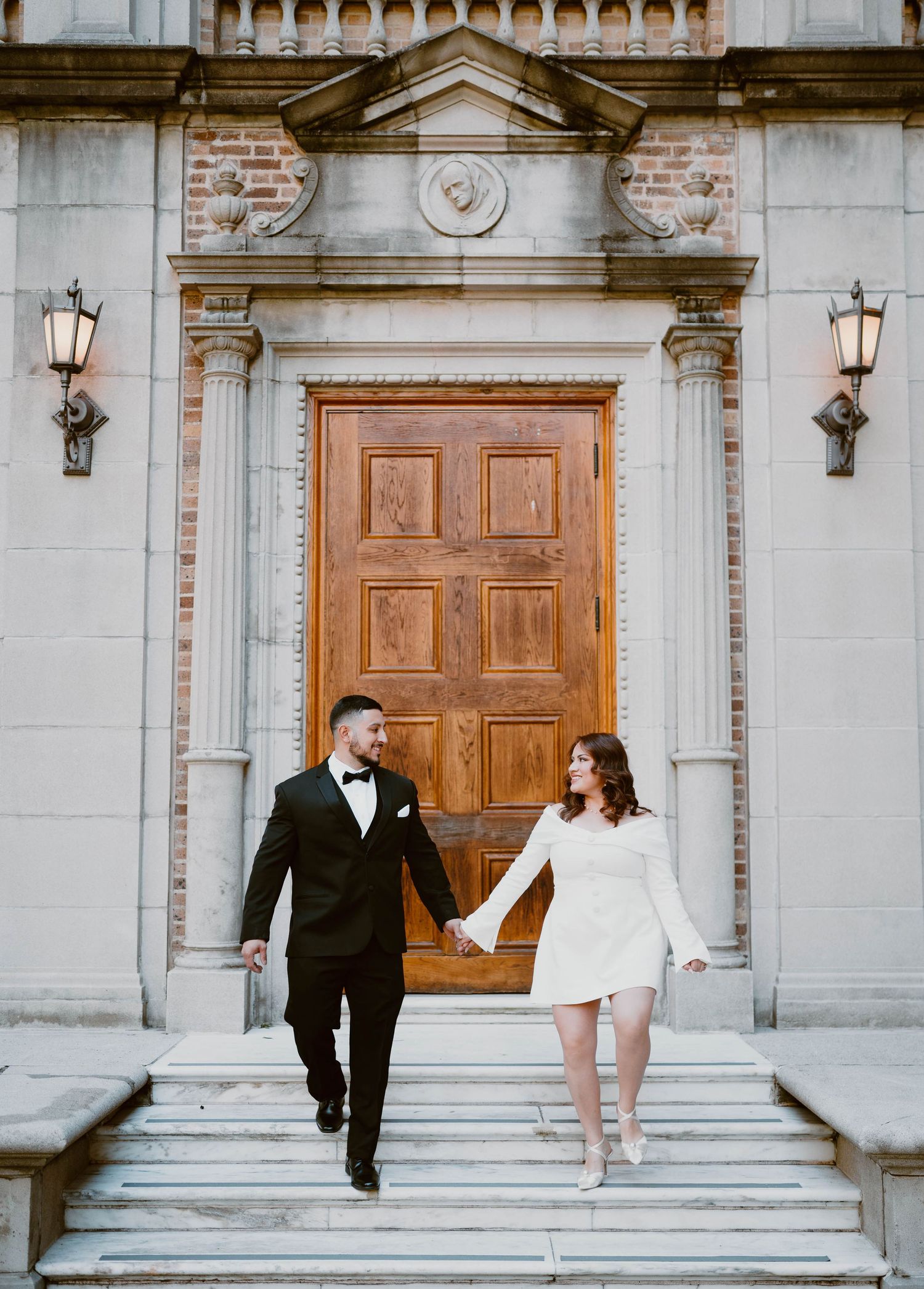 Couple poses playfully on elegant stone steps in formal attire during a romantic photoshoot.
