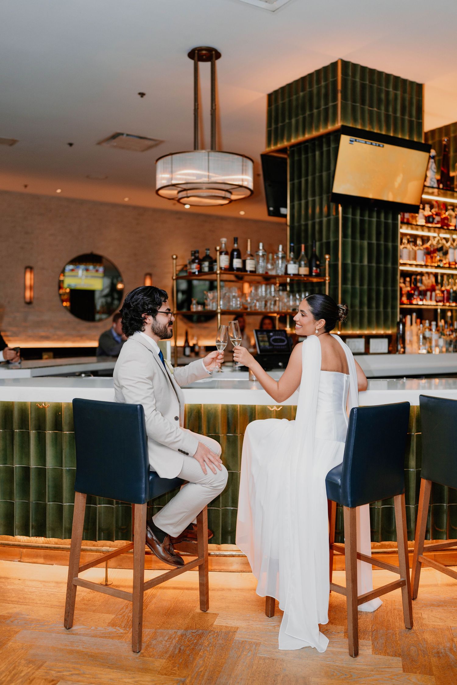 Couple toasting at modern bar with green tile and ambient lighting.