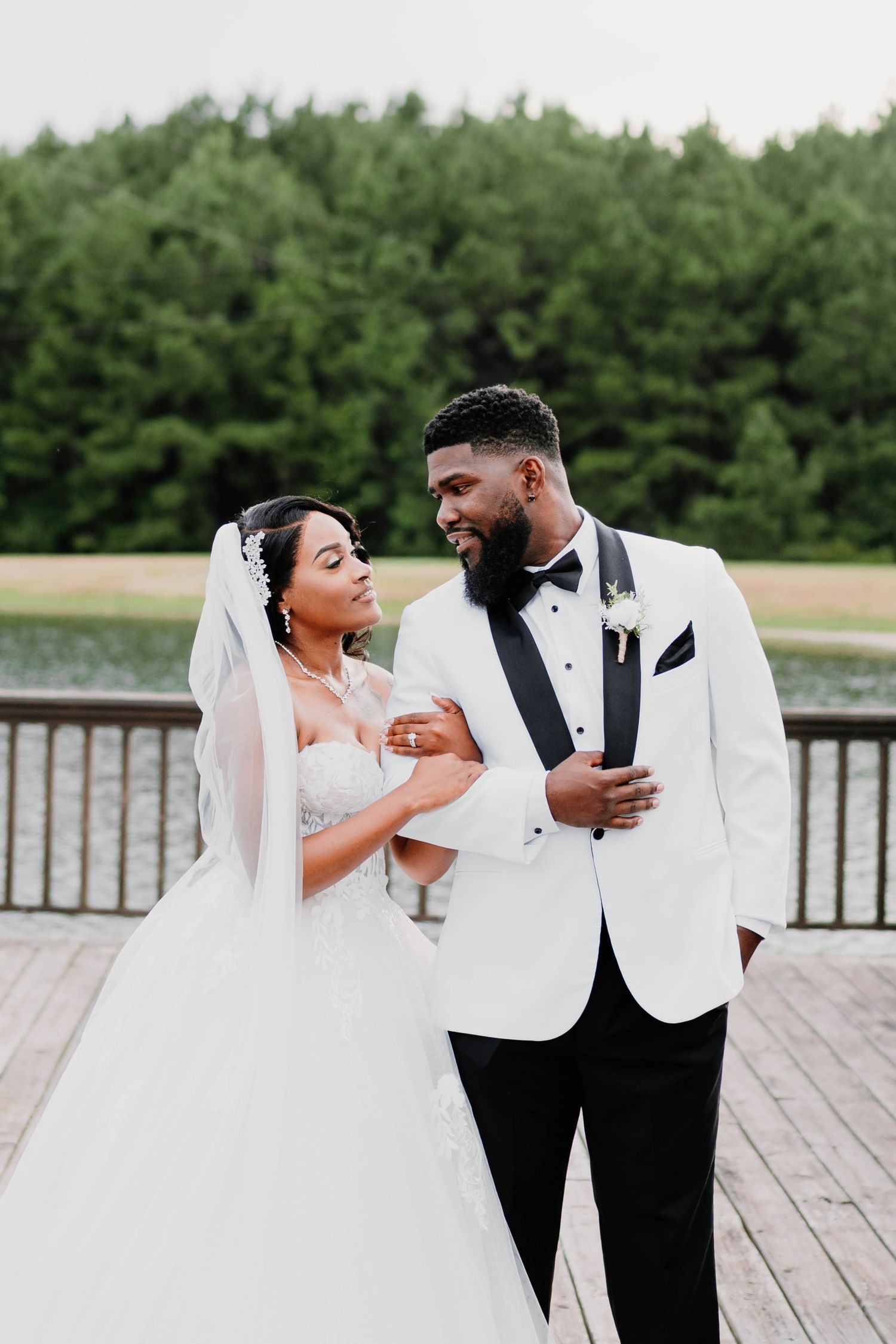 A happy couple shares joyful moments together on a wooden deck overlooking a lake during their wedding photoshoot.