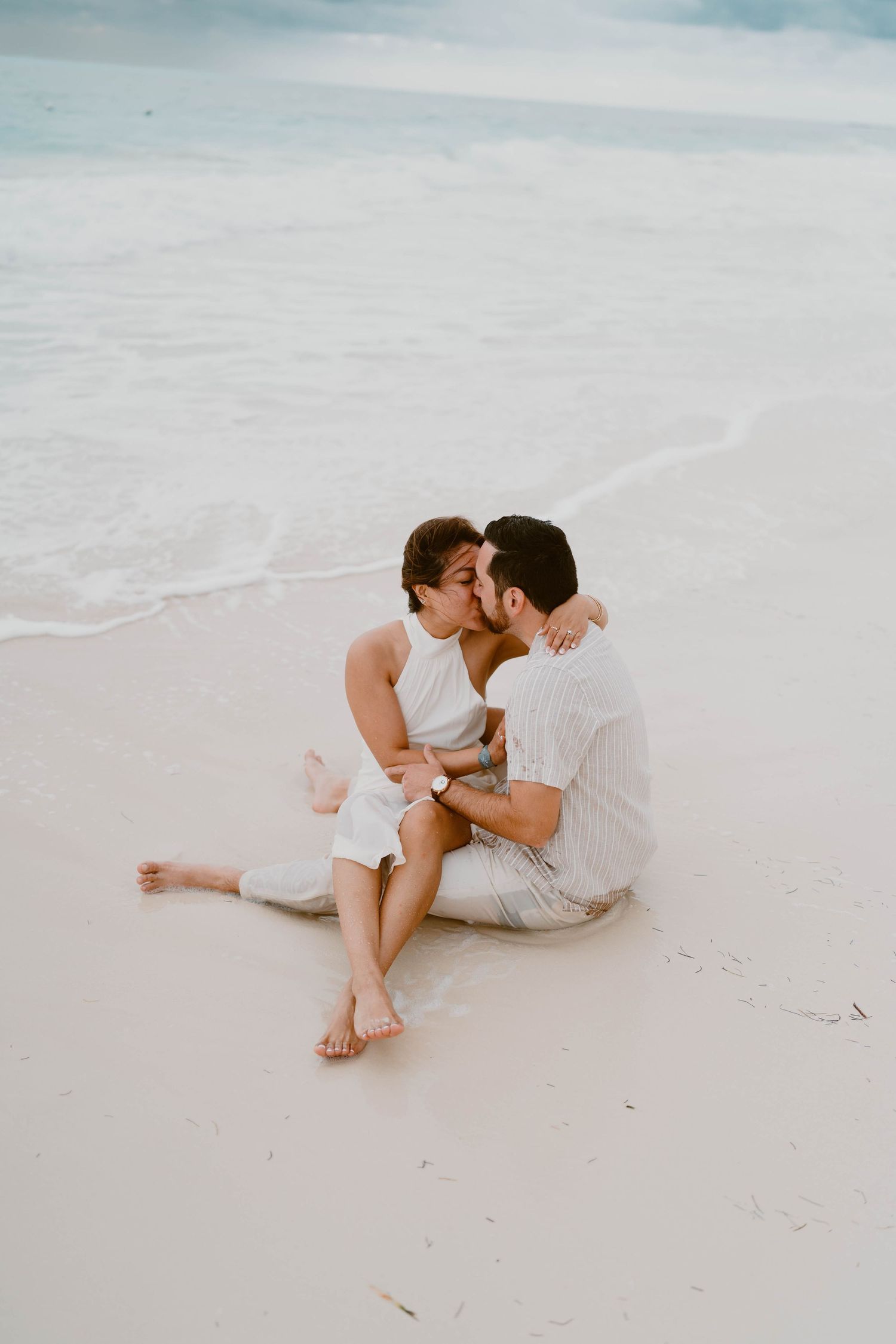 Couple shares intimate moments while sitting together on pristine white sand beach.