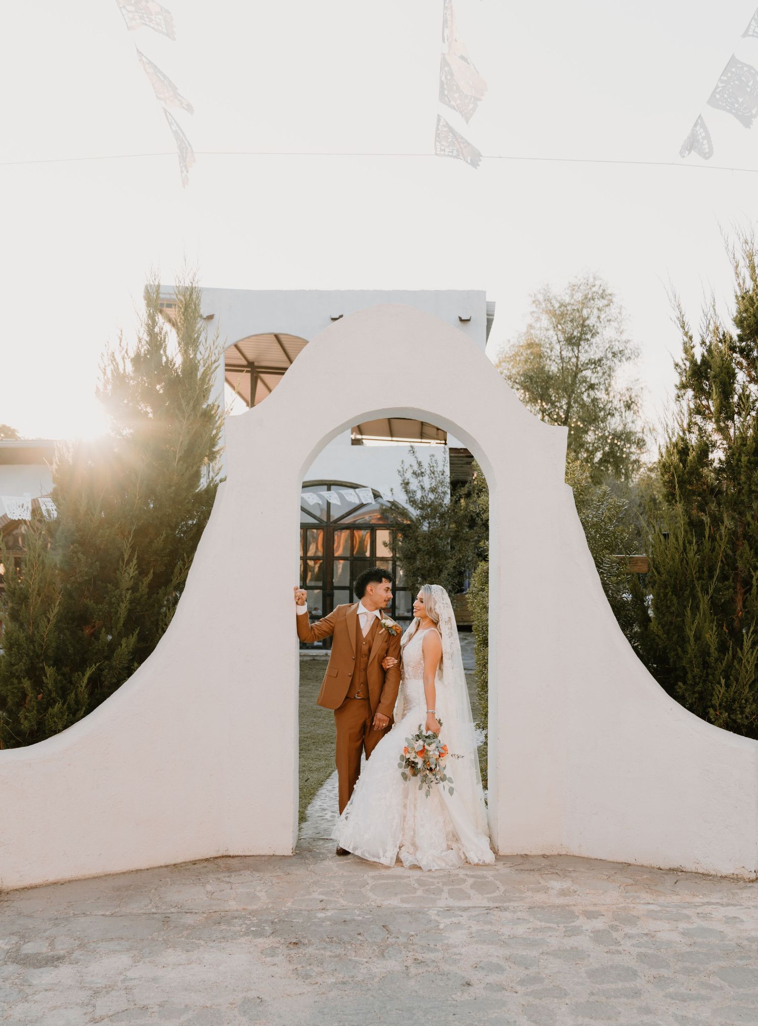 Wedding couple photographed through circular white architectural features at sunset.