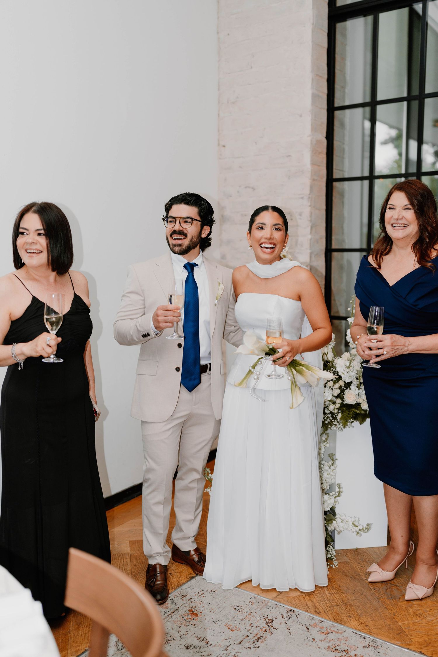 Wedding party members smile and raise glasses during a celebration toast in an elegant venue.