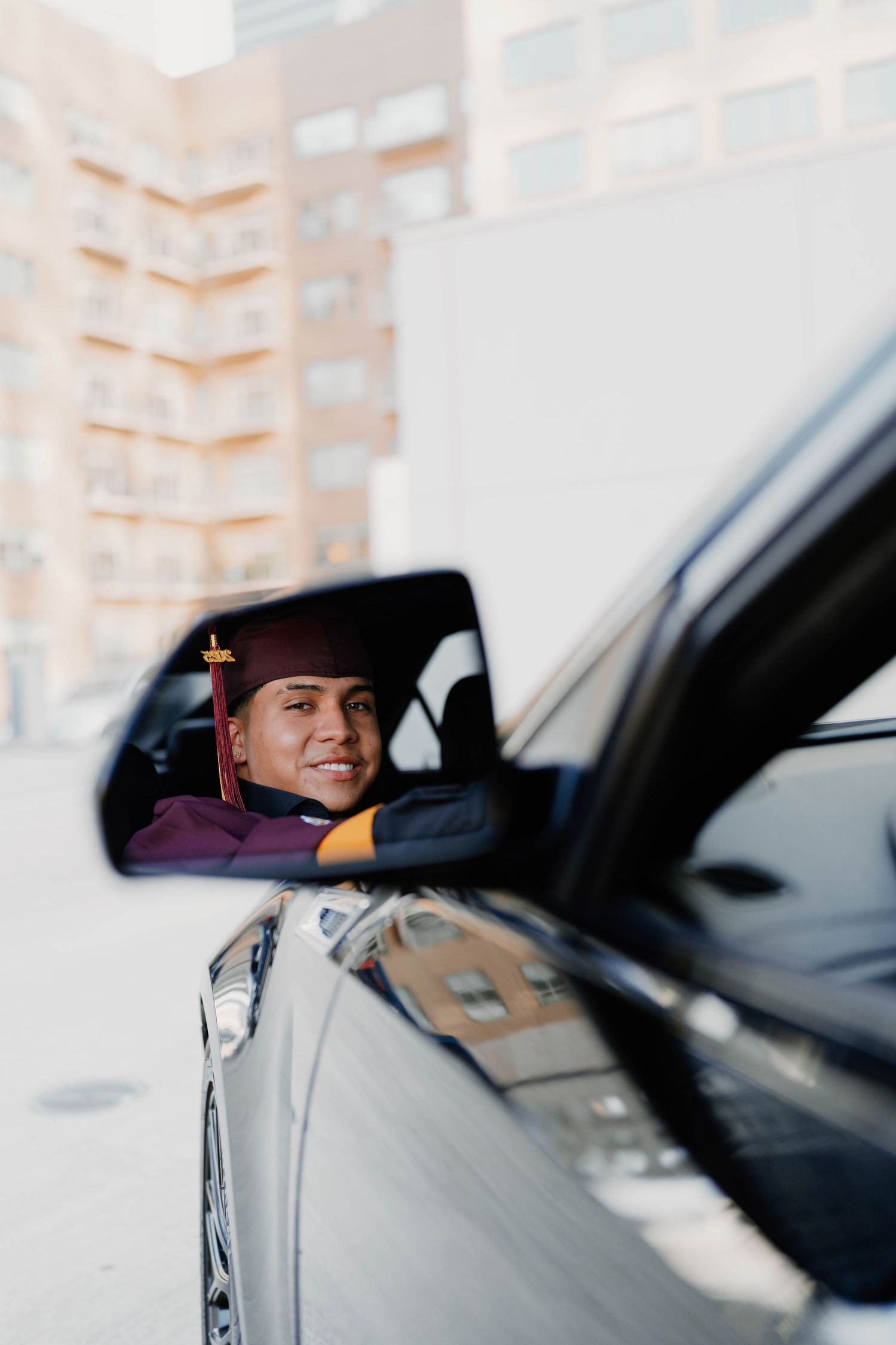 Candid graduation photos taken through car window with urban backdrop.