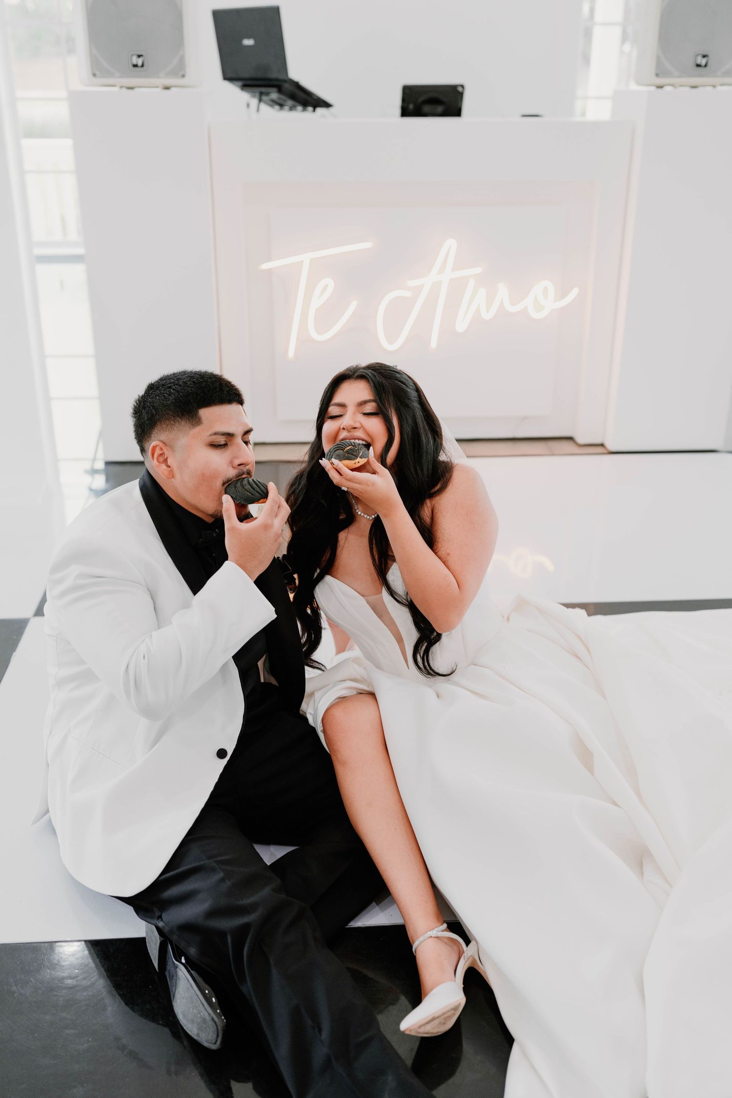 Romantic couple posing with neon 'Te Amo' sign in modern white studio setting.