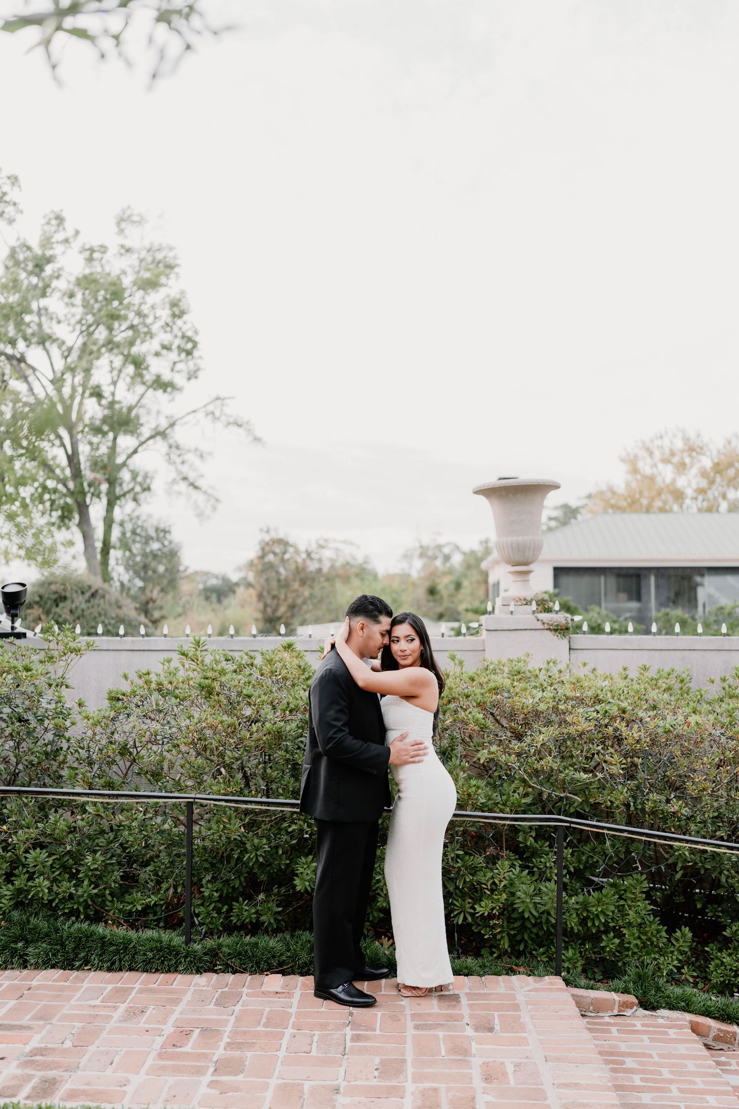 Couple poses on brick terrace with garden backdrop at sunset.