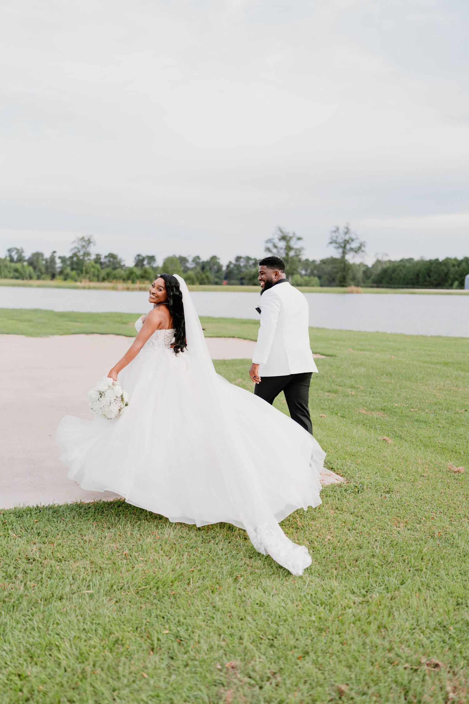 Newlyweds playfully run across a grassy field by the water.